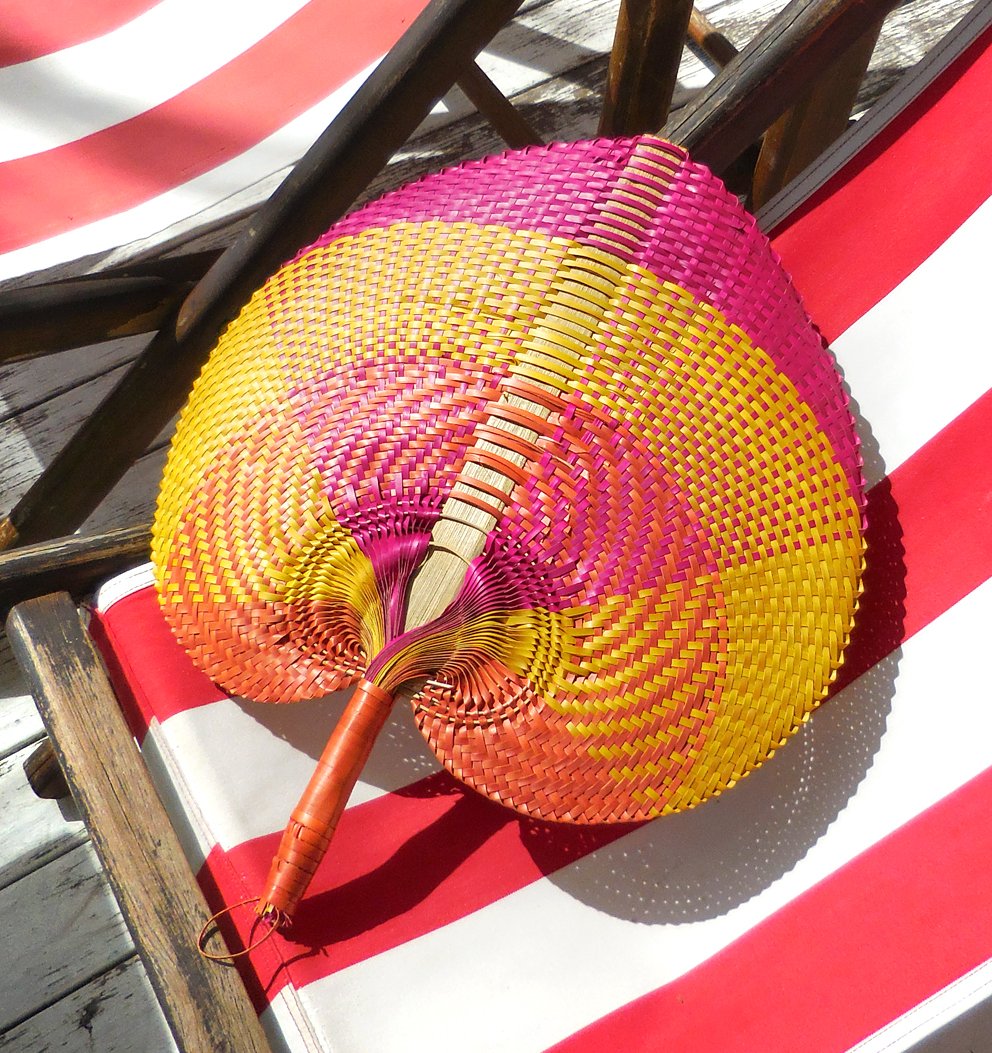 A beautifully handwoven Balinese fan made from Pandan straws, featuring intricate patterns and a large size, perfect for summer use and tropical decor.