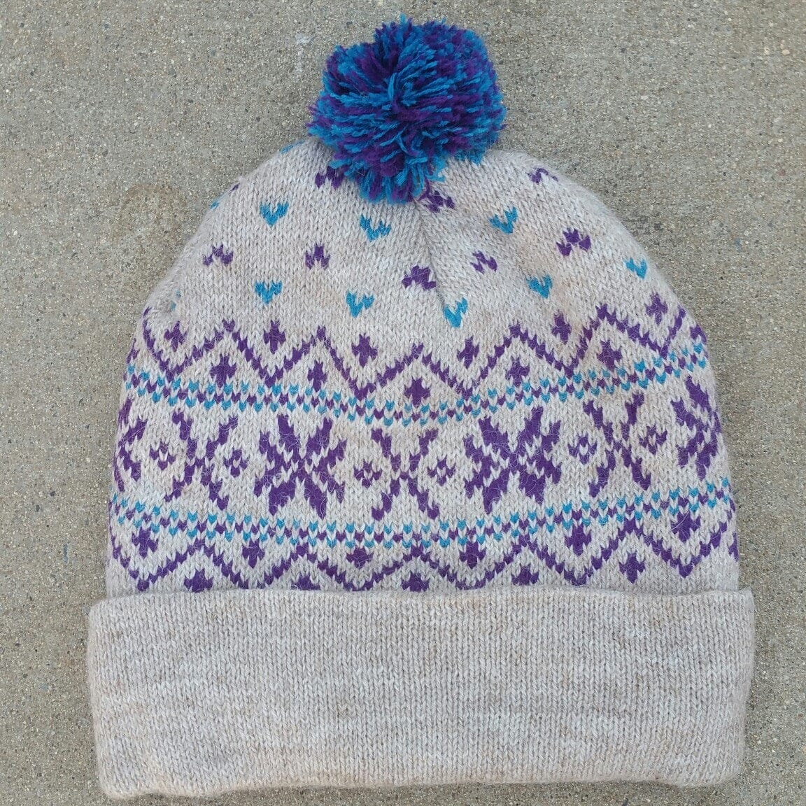 A vibrant Snowflake Pom-Pom Alpaca Hat featuring a soft SURI alpaca blend yarn with colorful pom-pom accents and a cozy microfiber lining.