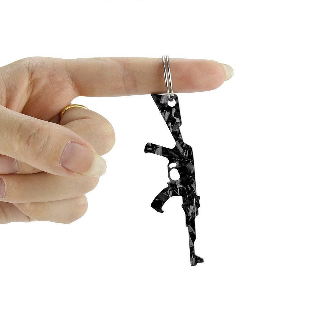 Forged carbon fiber keychain shaped like an AK-47, featuring a bottle opener and key ring, showcasing its sleek and durable design.