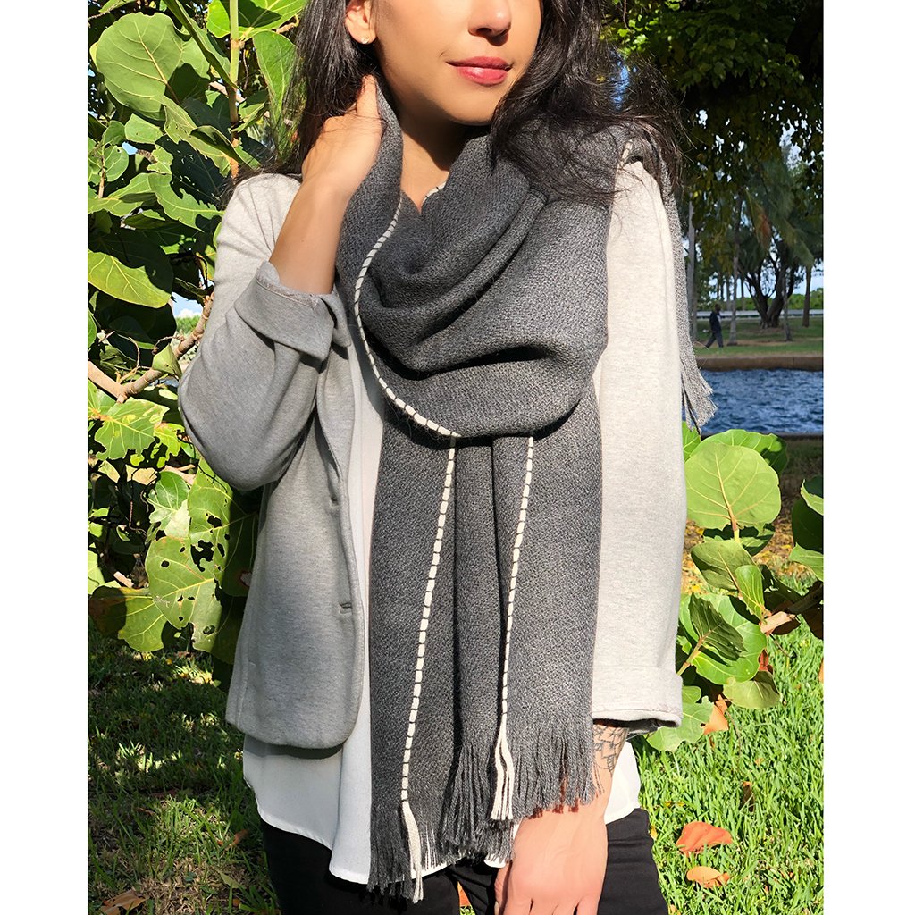 A luxurious Andes Charcoal Baby Alpaca Scarf featuring a charcoal gray color with a snow white edge, showcasing its soft texture and fringe details.