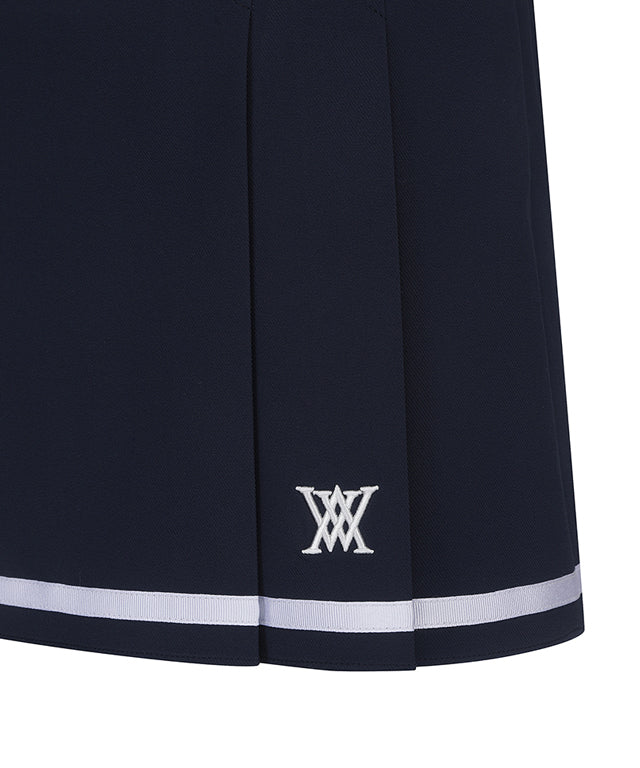 Navy A-line skirt with two-tier pleats, featuring a D-ring logo and color point tape at the hem.