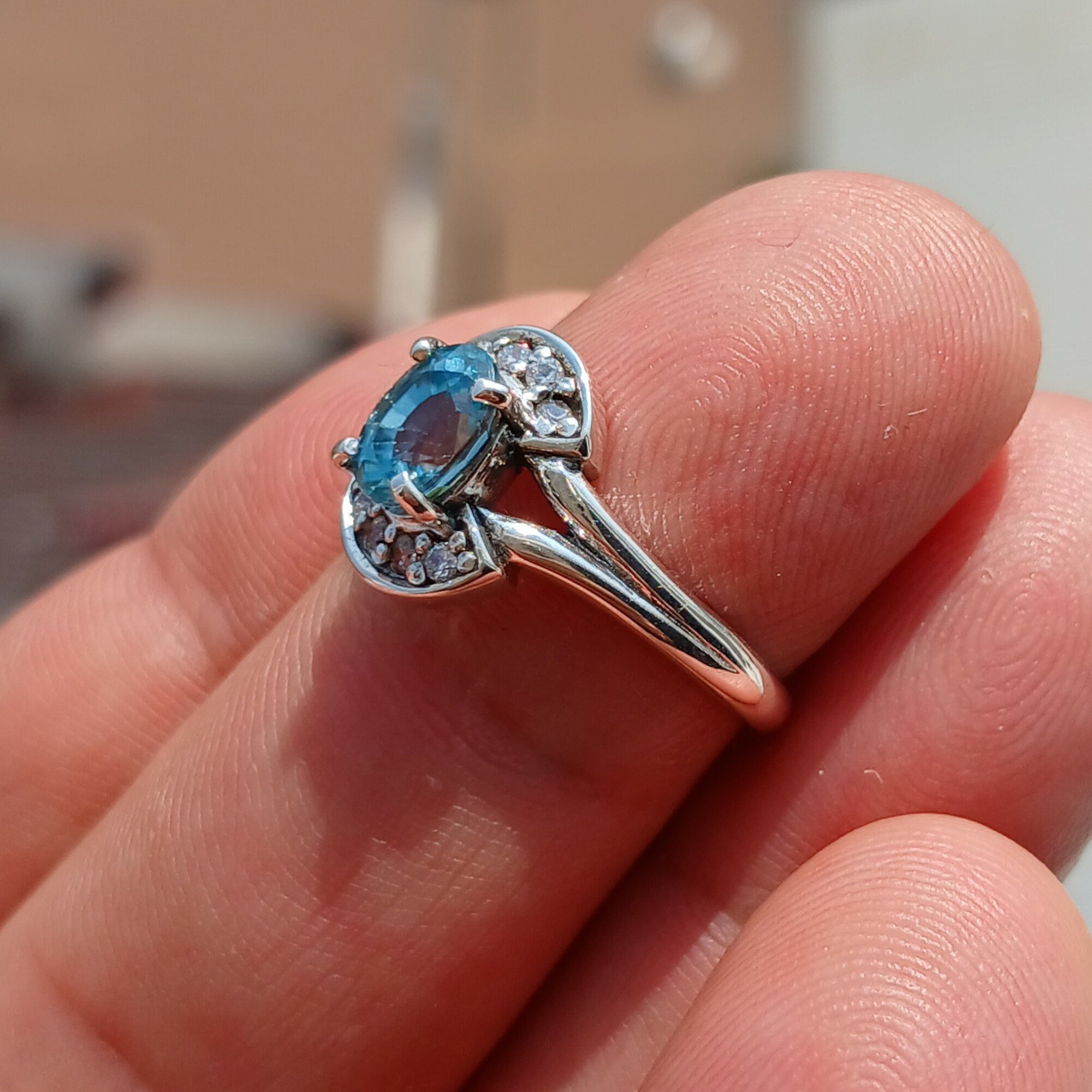Handmade sterling silver ring featuring a blue zircon gemstone surrounded by eight cubic zirconia stones, elegantly polished.