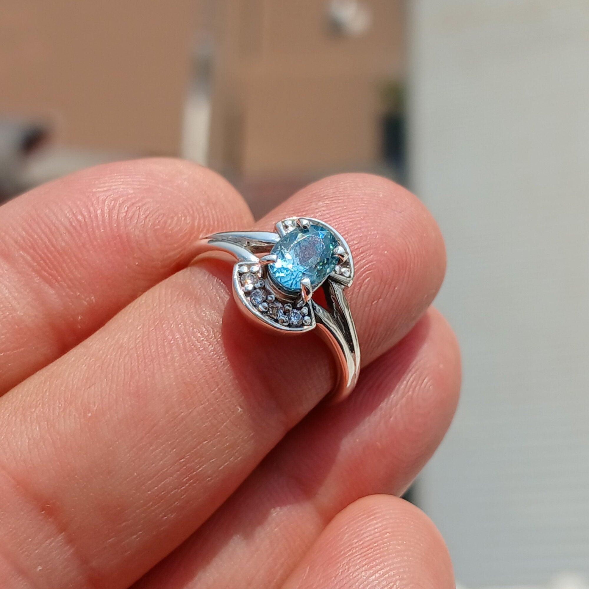 Handmade sterling silver ring featuring a blue zircon gemstone surrounded by eight cubic zirconia stones, elegantly polished.