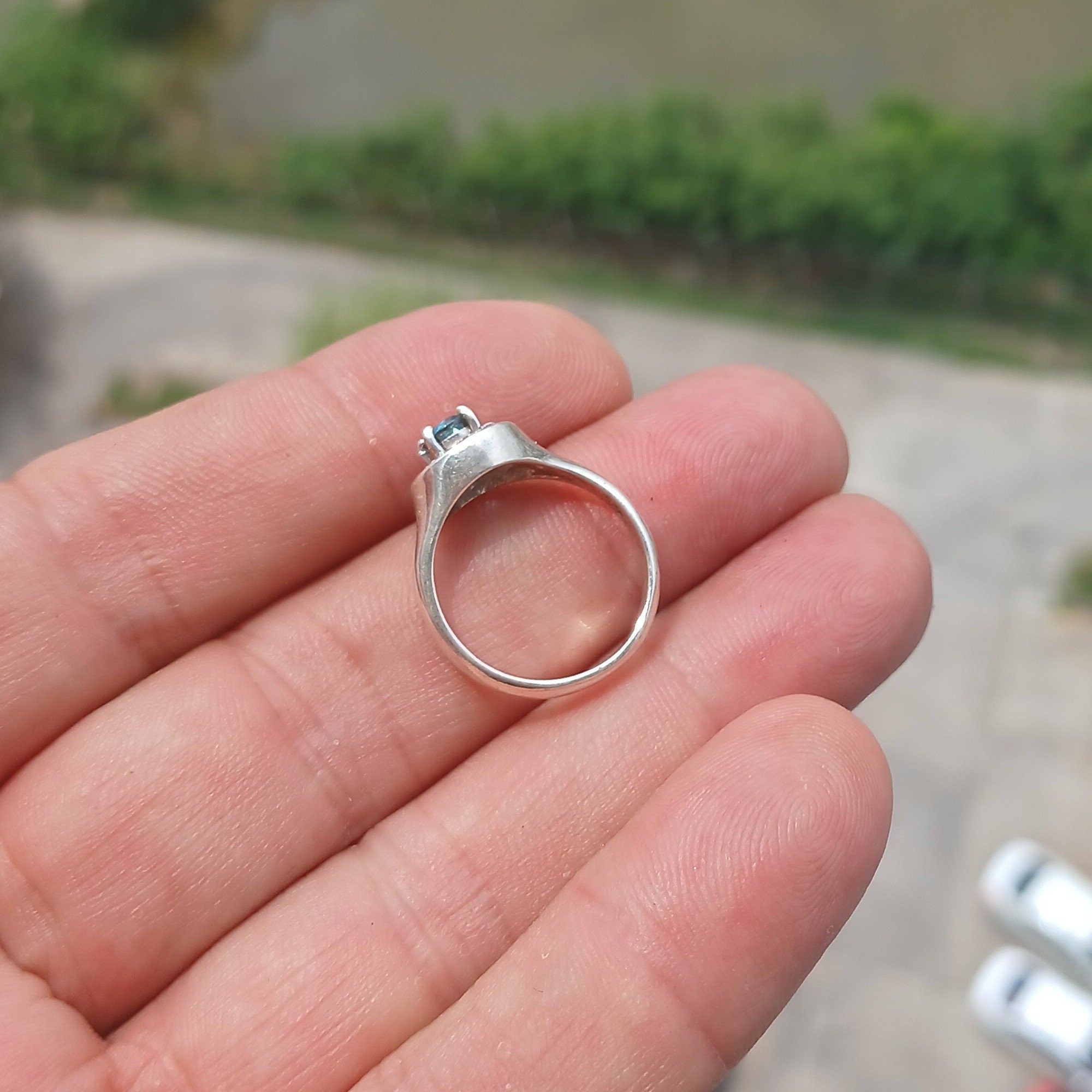 A stunning Blue Zircon Ring featuring a natural blue Zircon stone surrounded by 13 white CZ stones, set in polished sterling silver.