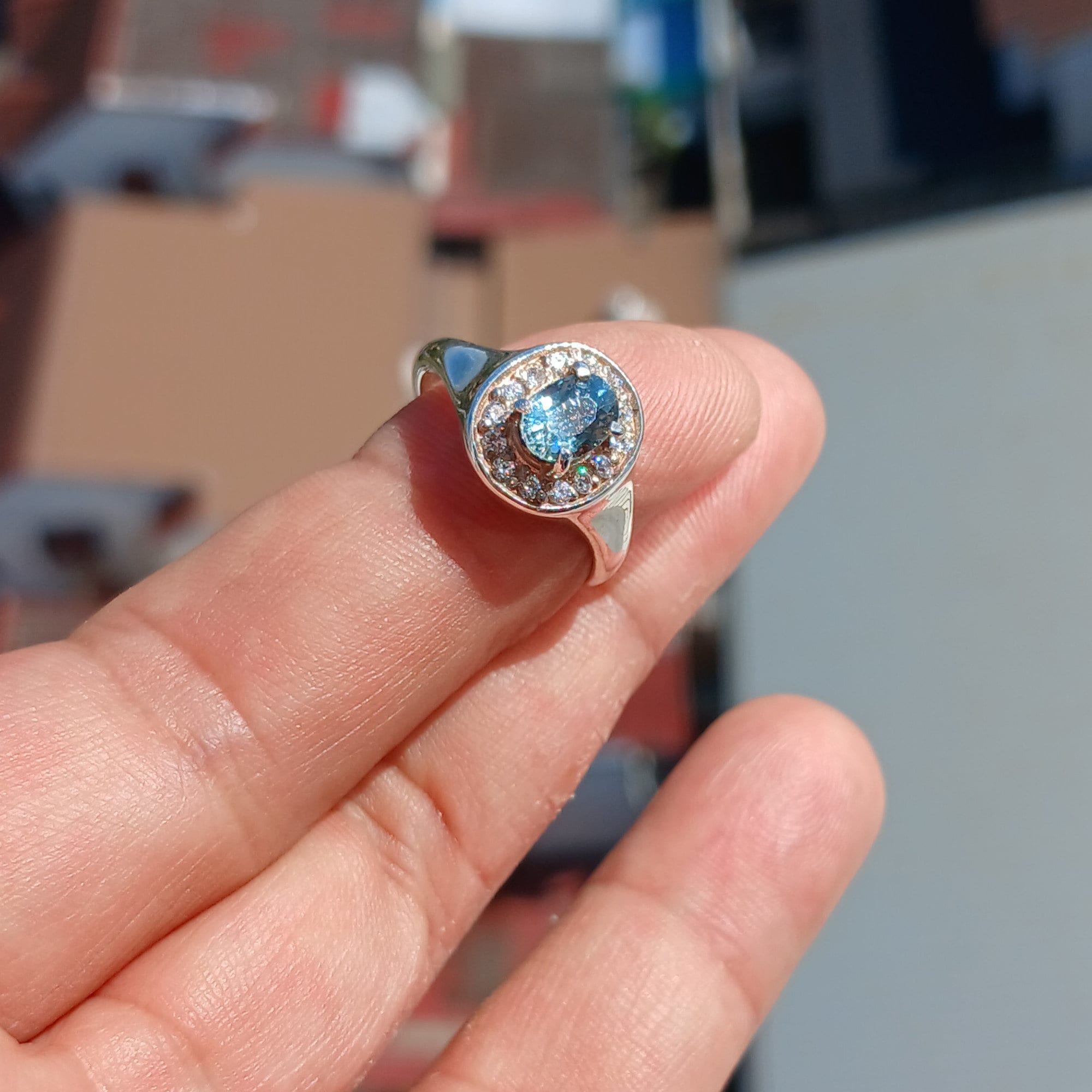 A stunning Blue Zircon Ring featuring an oval cut blue zircon centerpiece set in a polished sterling silver band, surrounded by 14 white cubic zirconia stones.