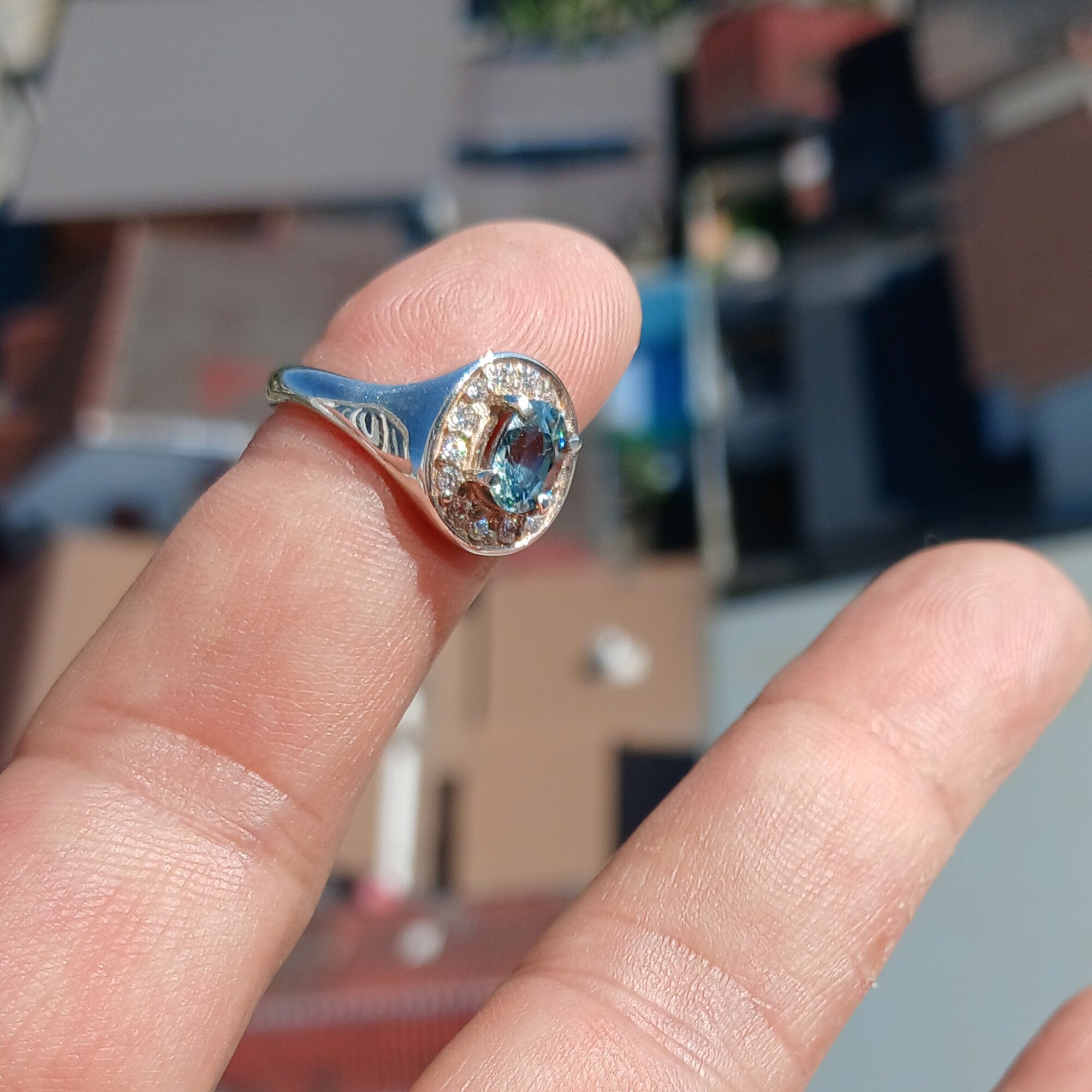 A stunning Blue Zircon Ring featuring an oval cut blue zircon centerpiece set in a polished sterling silver band, surrounded by 14 white cubic zirconia stones.