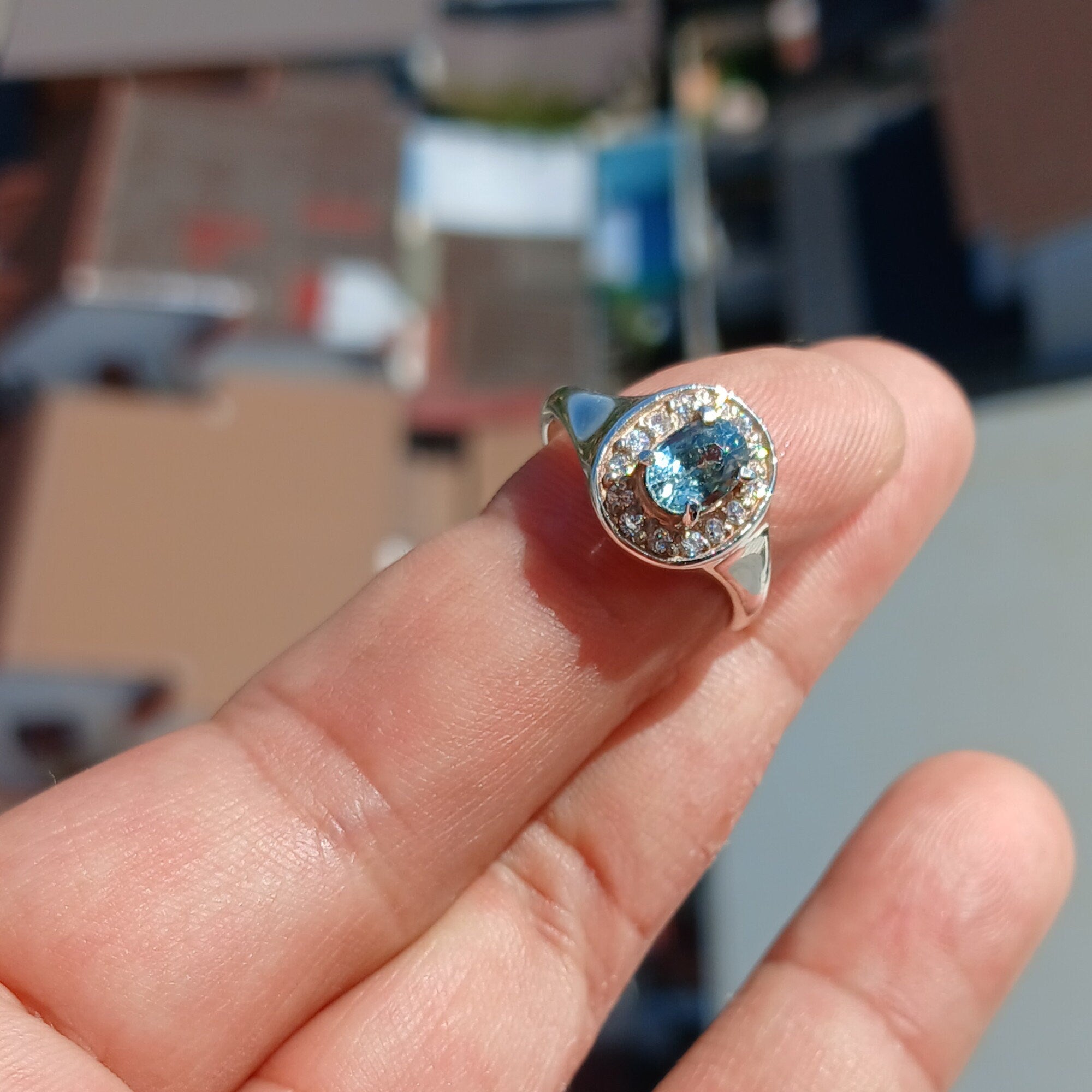 A stunning Blue Zircon Ring featuring an oval cut blue zircon centerpiece set in a polished sterling silver band, surrounded by 14 white cubic zirconia stones.