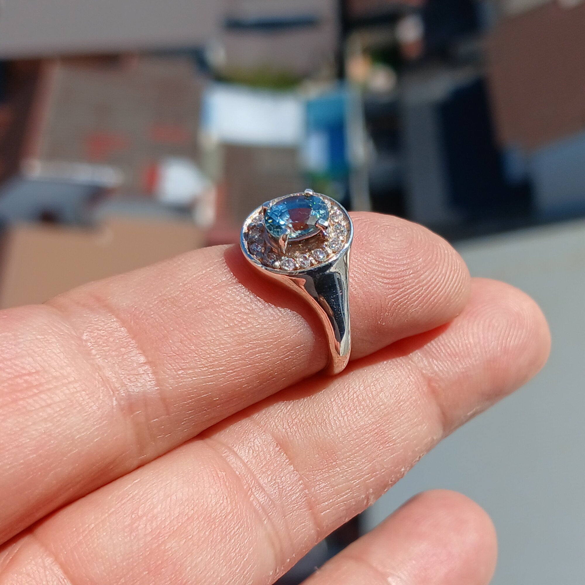 A stunning Blue Zircon Ring featuring an oval cut blue zircon centerpiece set in a polished sterling silver band, surrounded by 14 white cubic zirconia stones.