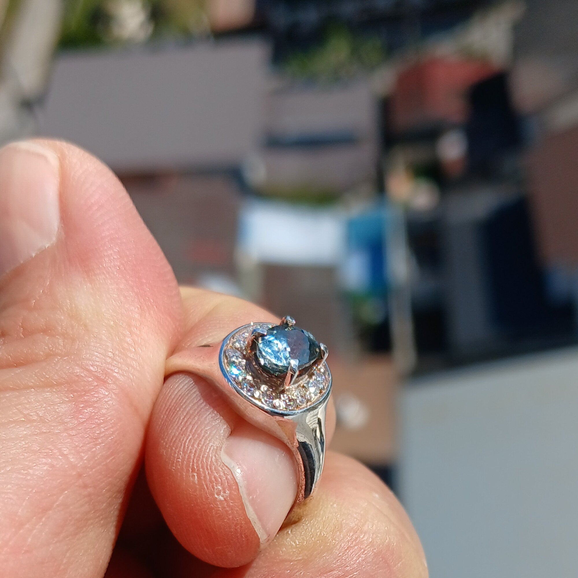 A stunning Blue Zircon Ring featuring an oval cut blue zircon centerpiece set in a polished sterling silver band, surrounded by 14 white cubic zirconia stones.