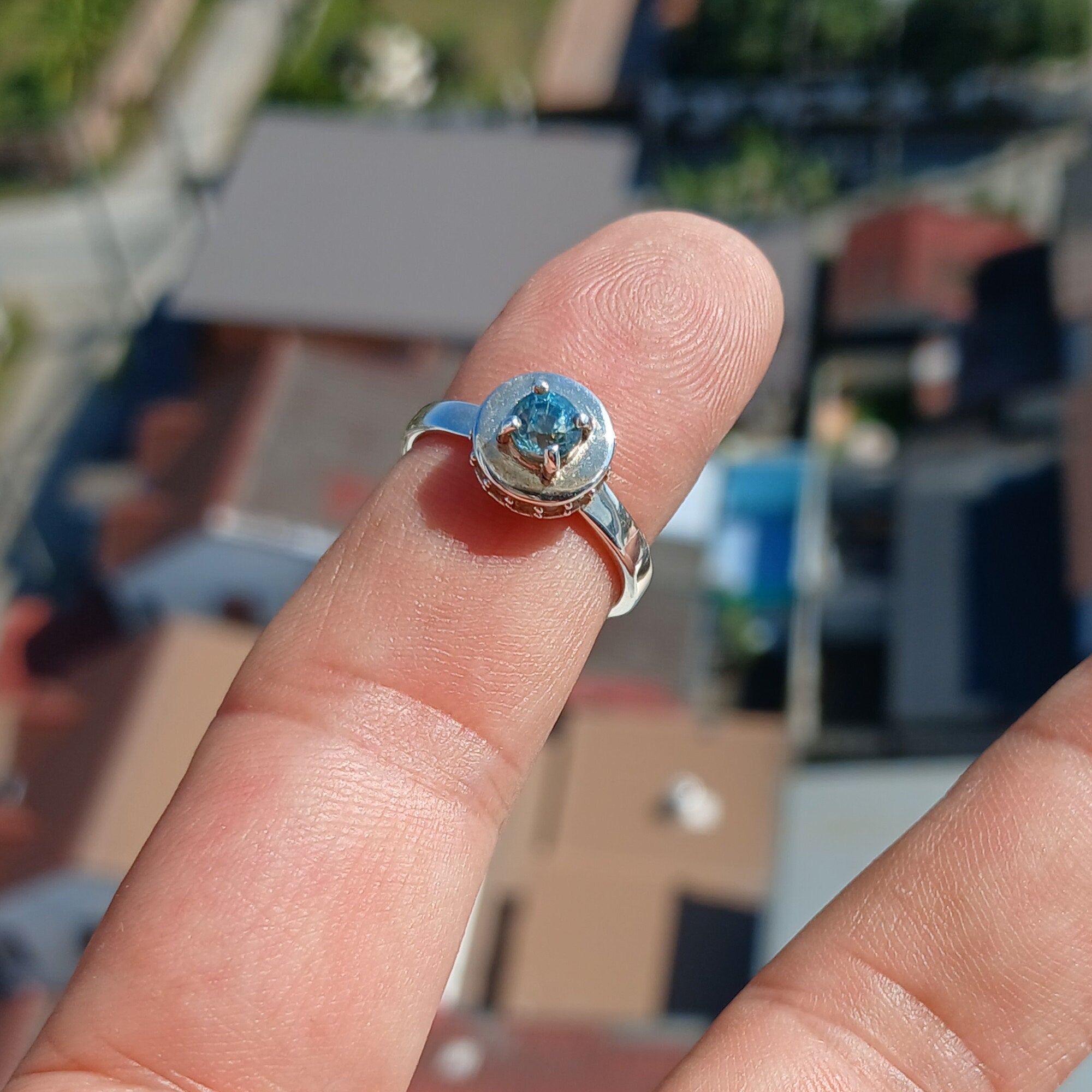 A stunning Blue Zircon Ring featuring a round cut blue gemstone at the center, surrounded by 14 sparkling white CZ stones, set in a polished sterling silver band.