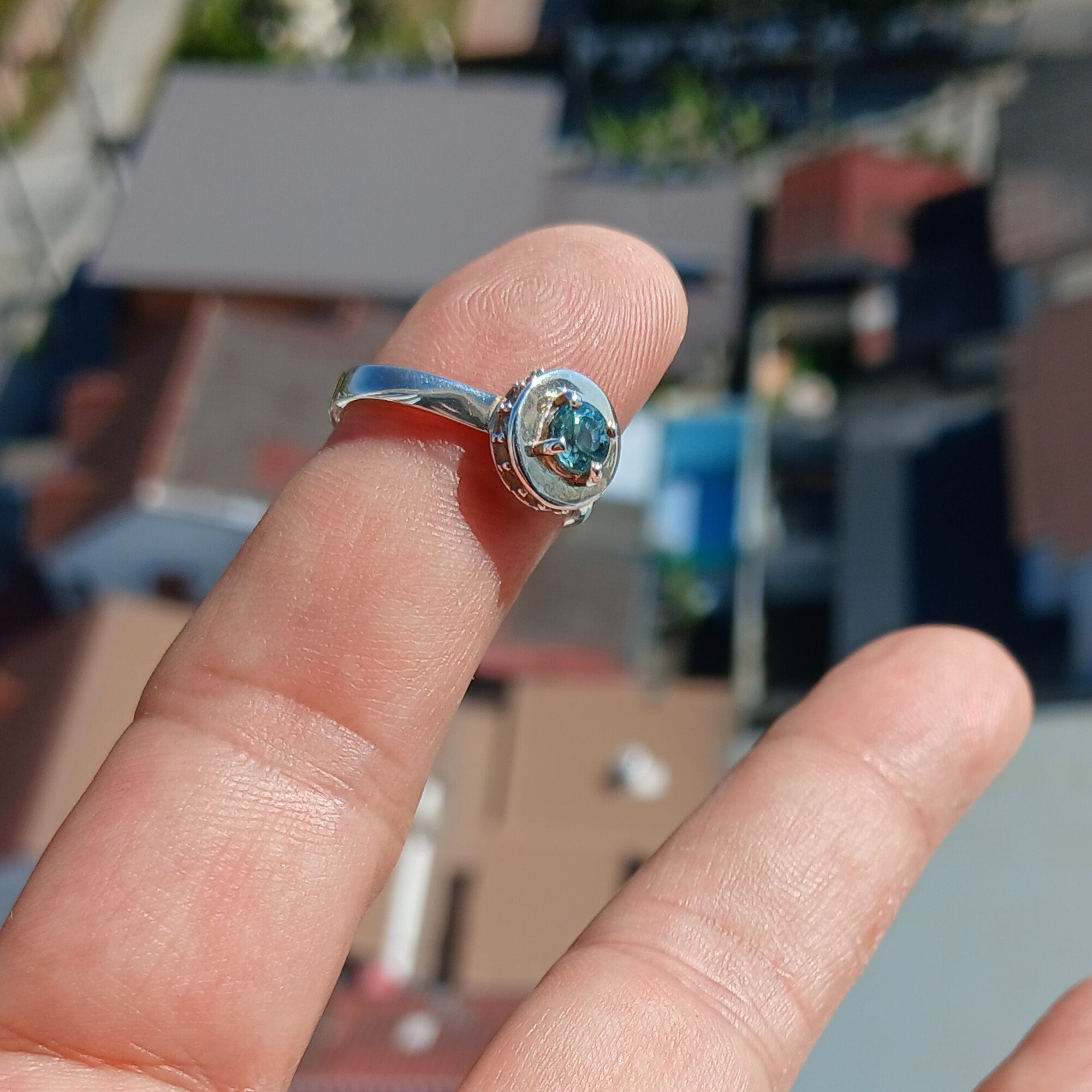 A stunning Blue Zircon Ring featuring a round cut blue gemstone at the center, surrounded by 14 sparkling white CZ stones, set in a polished sterling silver band.
