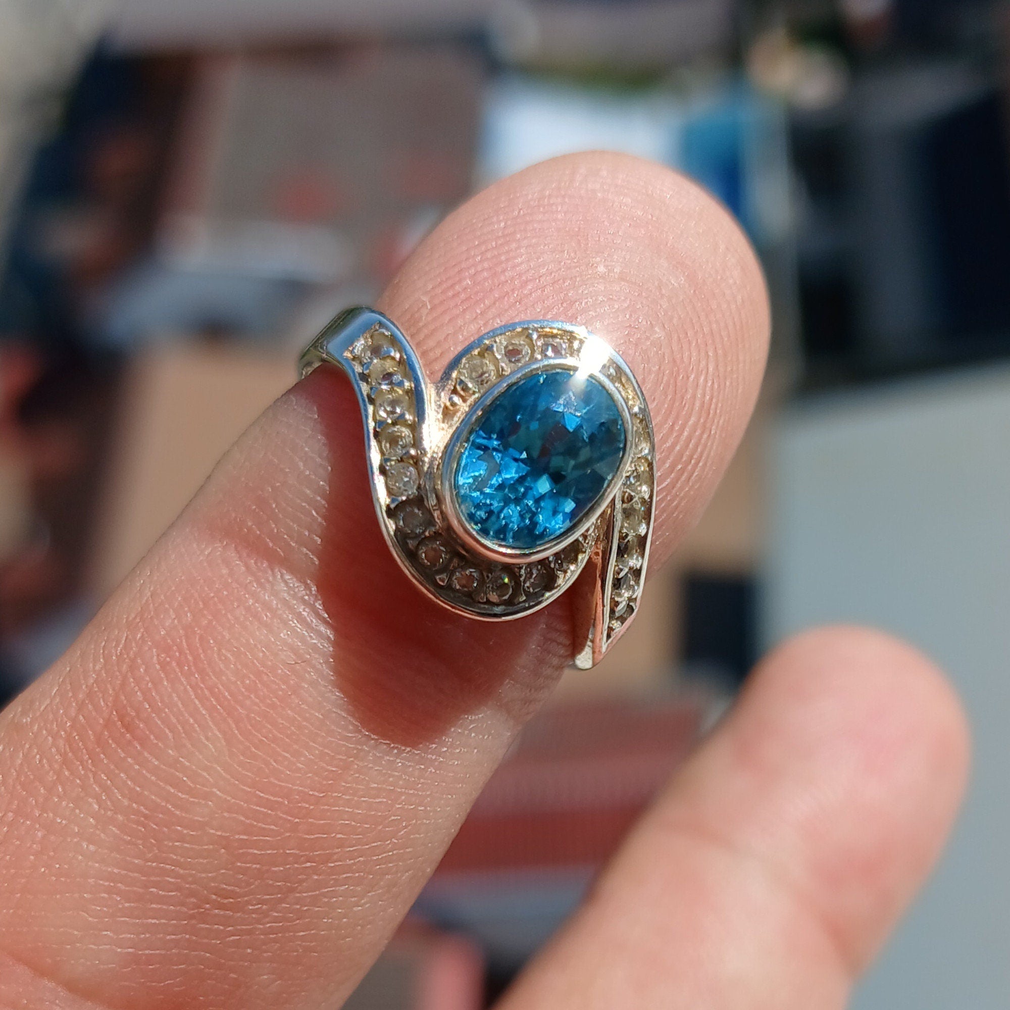 A stunning Blue Zircon Ring featuring an oval cut blue gemstone surrounded by 22 white CZ stones, set in polished sterling silver.
