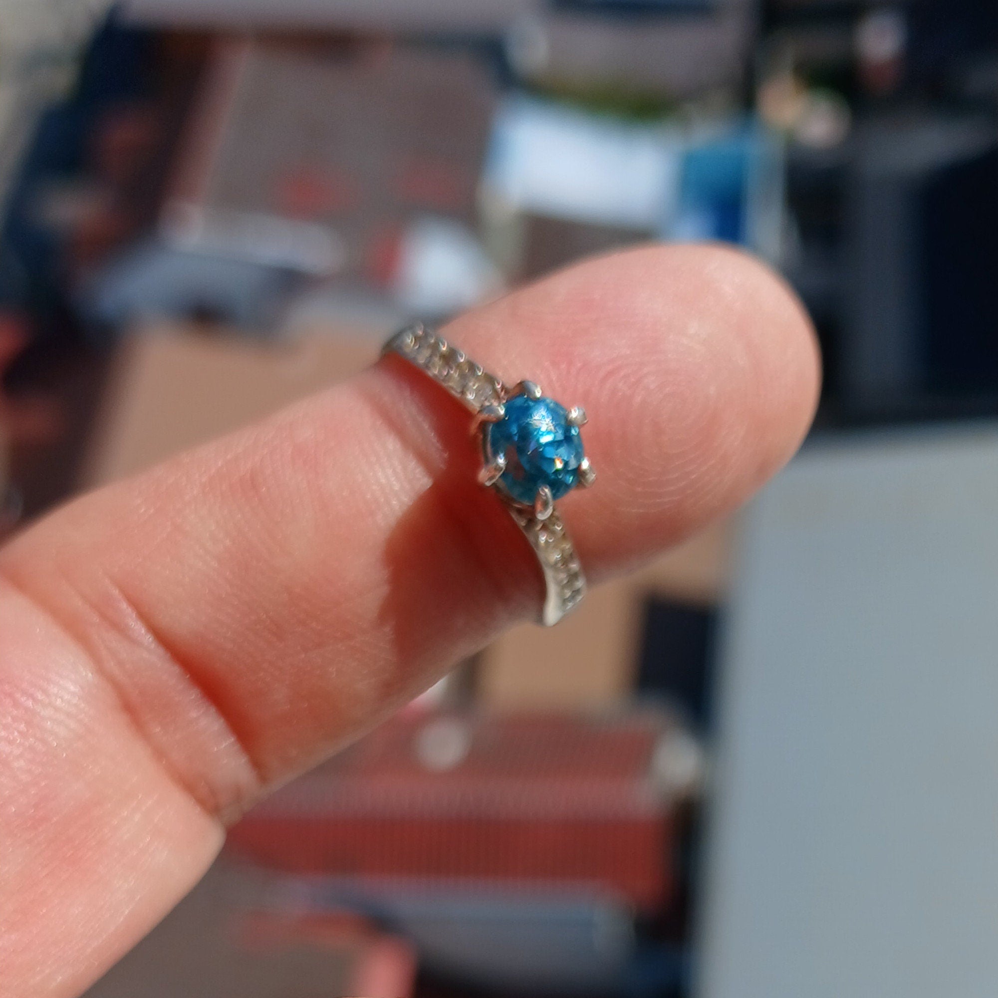 A beautiful Blue Zircon Ring featuring a round cut blue zircon gemstone surrounded by white cubic zirconia stones, set in polished sterling silver.