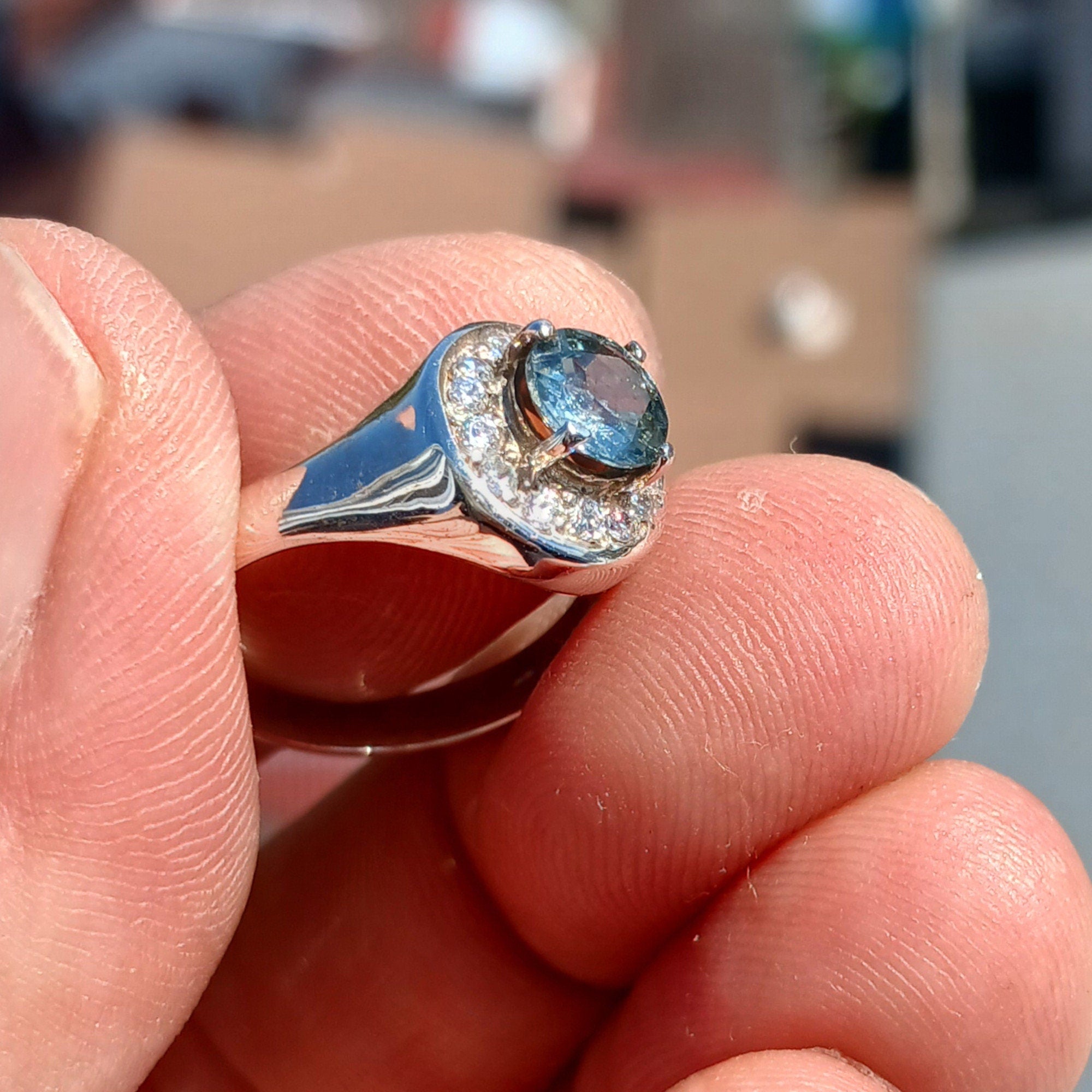 A stunning Blue Zircon Ring featuring a round cut blue zircon set in polished sterling silver, surrounded by 14 white CZ stones.