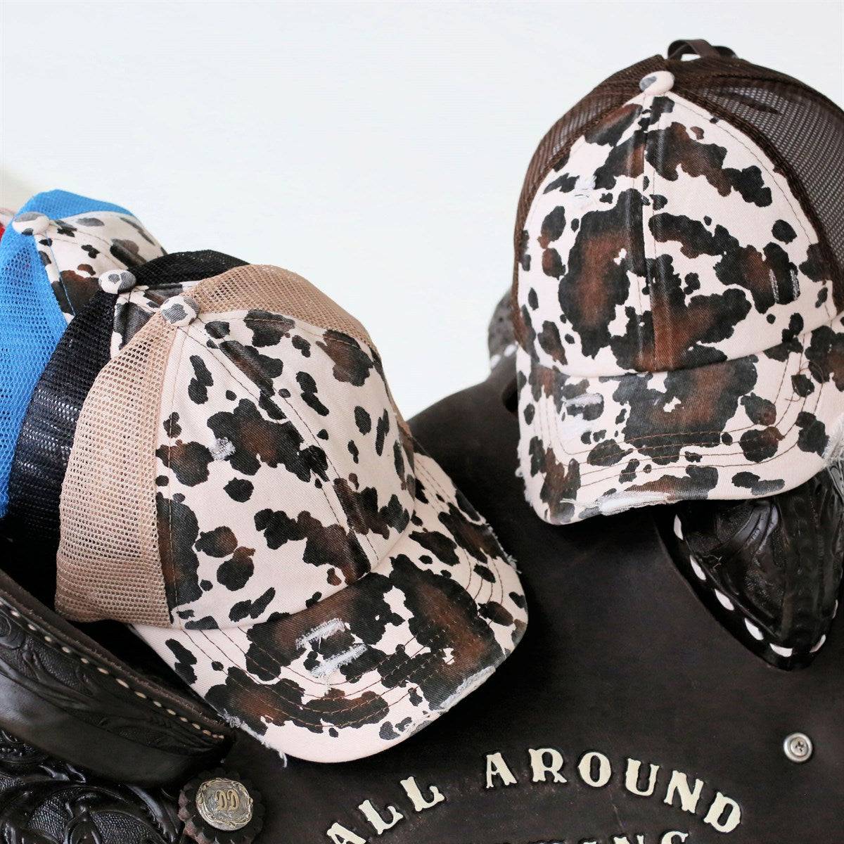 CC Cow Print Pony Hat featuring criss-cross elastic for ponytails, soft cotton material, and adjustable velcro strap.