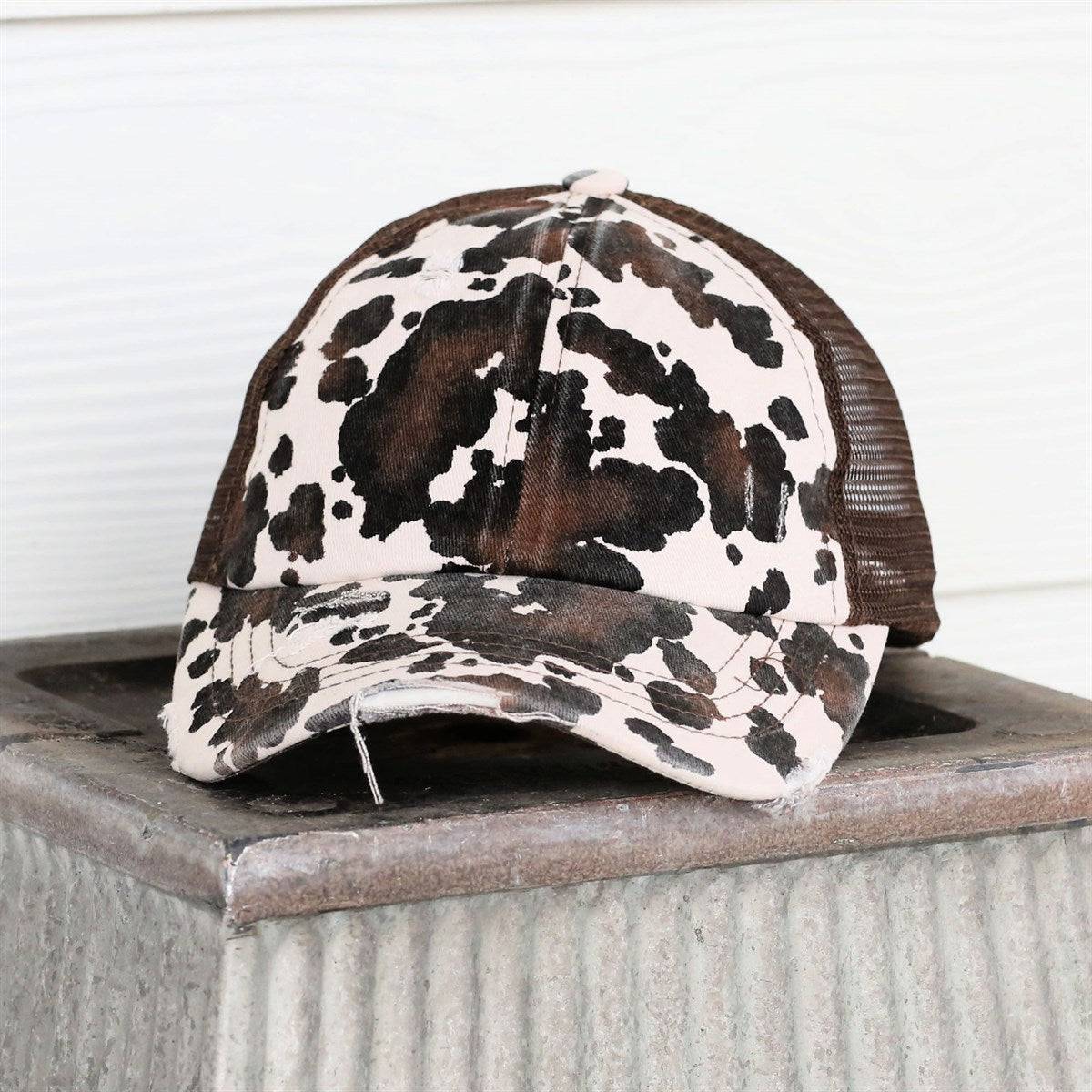 CC Cow Print Pony Hat featuring criss-cross elastic for ponytails, soft cotton material, and adjustable velcro strap.