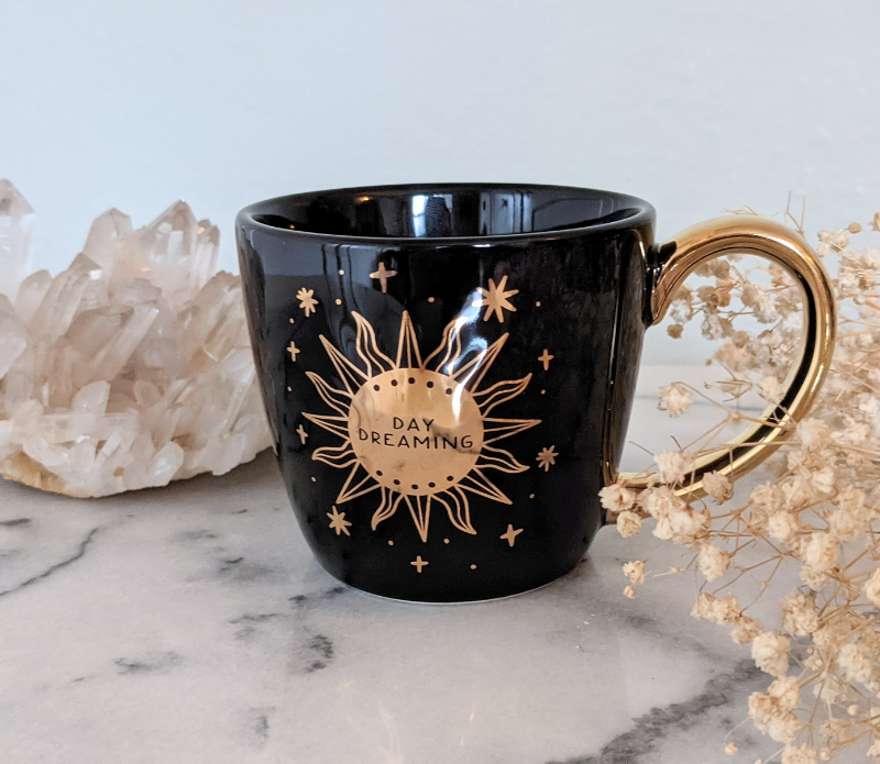 Celestial Tea Set featuring a mystical tea towel, a ceramic mug with gold designs, and a brass sun spoon, perfect for herbal tea rituals.