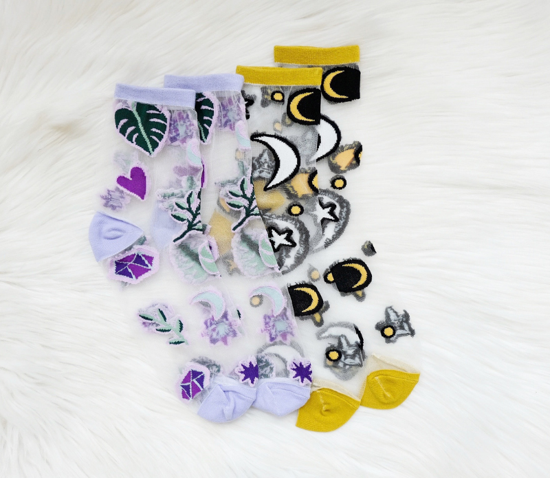 A pair of stylish embroidered mesh ankle socks featuring celestial designs with moons, stars, and botanical motifs in lavender and sunshine yellow trims.