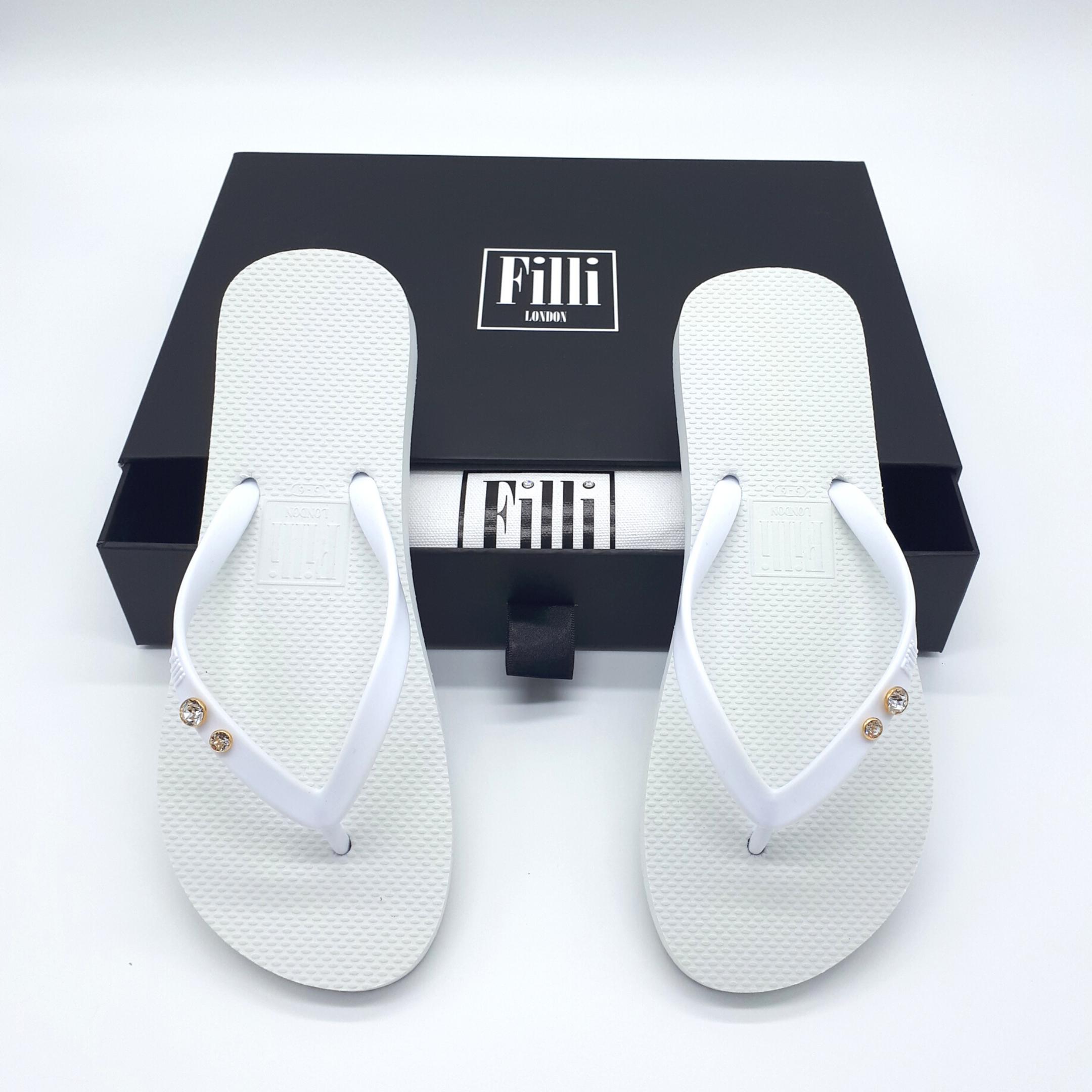 Filli London Crystal Diamond White Luxury Flip Flops featuring Swarovski® crystals in gold and silver settings, elegantly displayed in a cotton shoe bag.