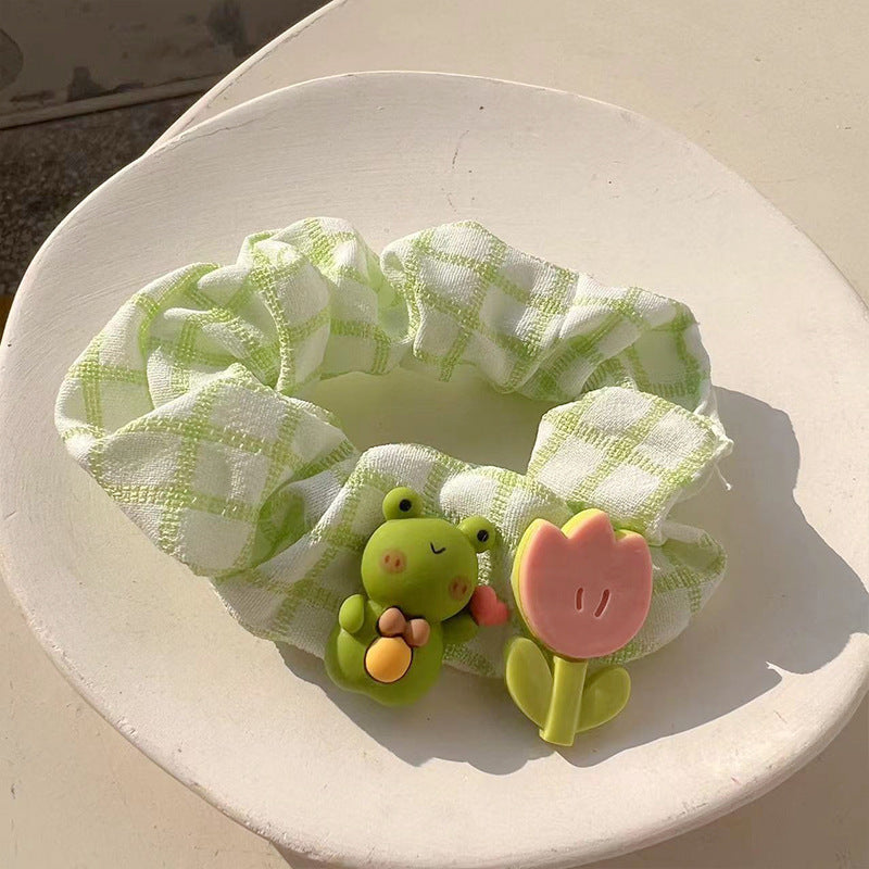 A charming green frog hair tie featuring a whimsical design, perfect for adding playful elegance to hairstyles.