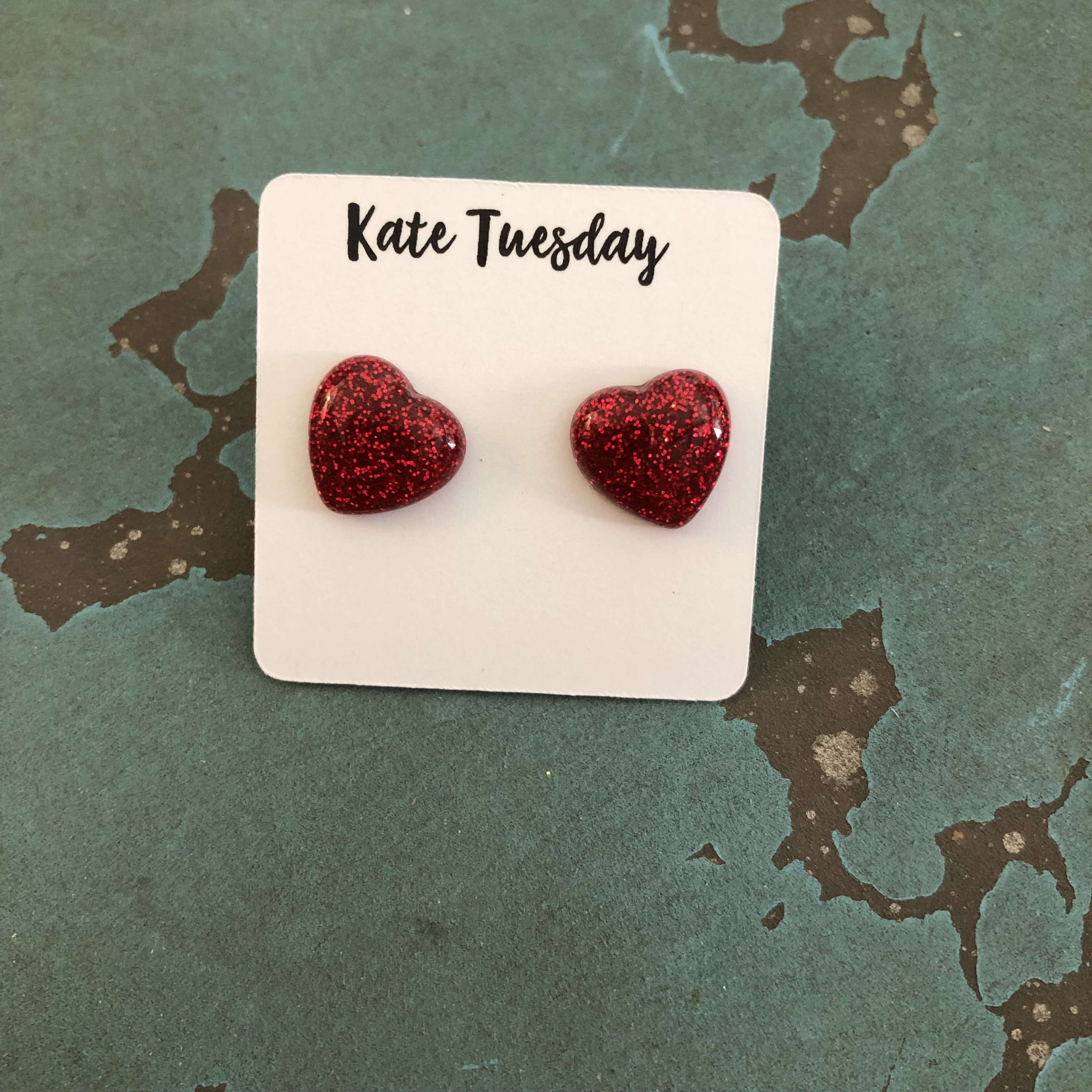 A pair of glittery red heart stud earrings with a shiny finish, showcasing their vibrant color and elegant design.