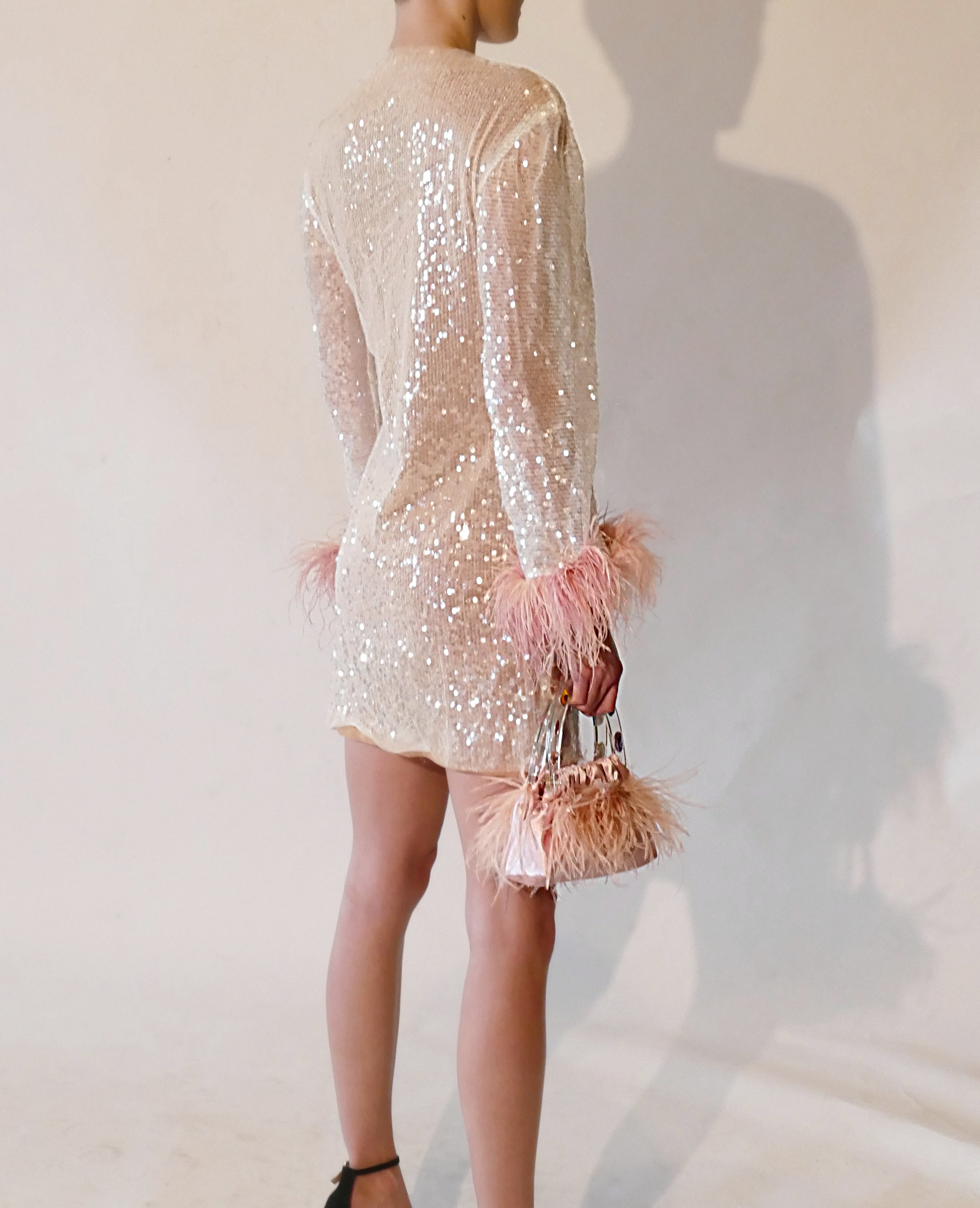 A stunning handmade party dress featuring sequins and feather trim, with long bell sleeves and a chic vegan leather design.