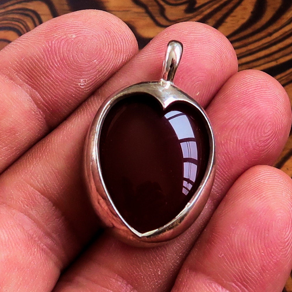 A stunning heart pendant made of sterling silver featuring a vibrant orange Agate Cabochon, showcasing its unique design and quality craftsmanship.
