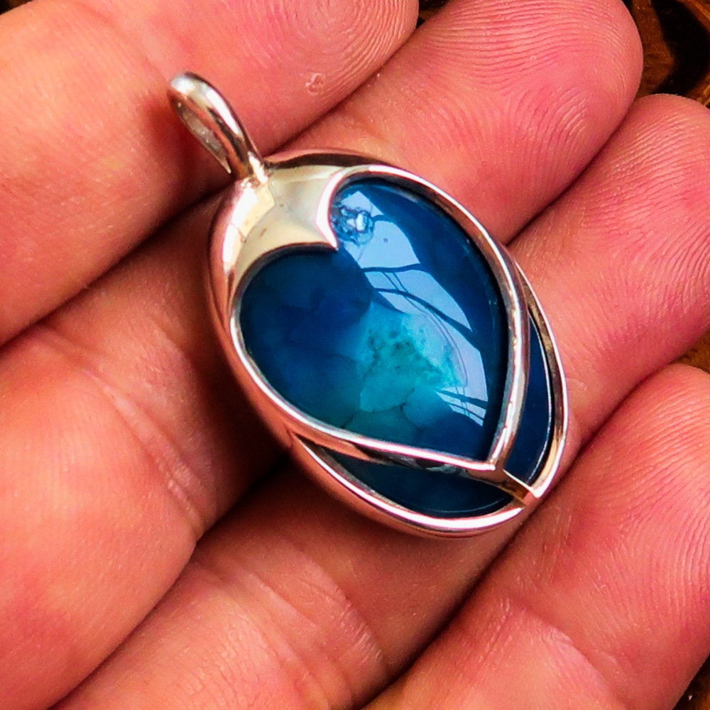 A beautiful heart-shaped sterling silver pendant featuring a blue agate cabochon, showcasing intricate craftsmanship and elegant design.
