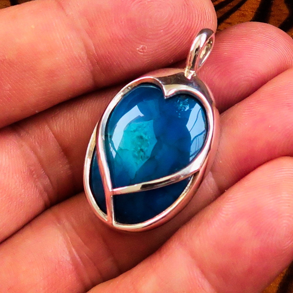 A beautiful heart-shaped sterling silver pendant featuring a blue agate cabochon, showcasing intricate craftsmanship and elegant design.