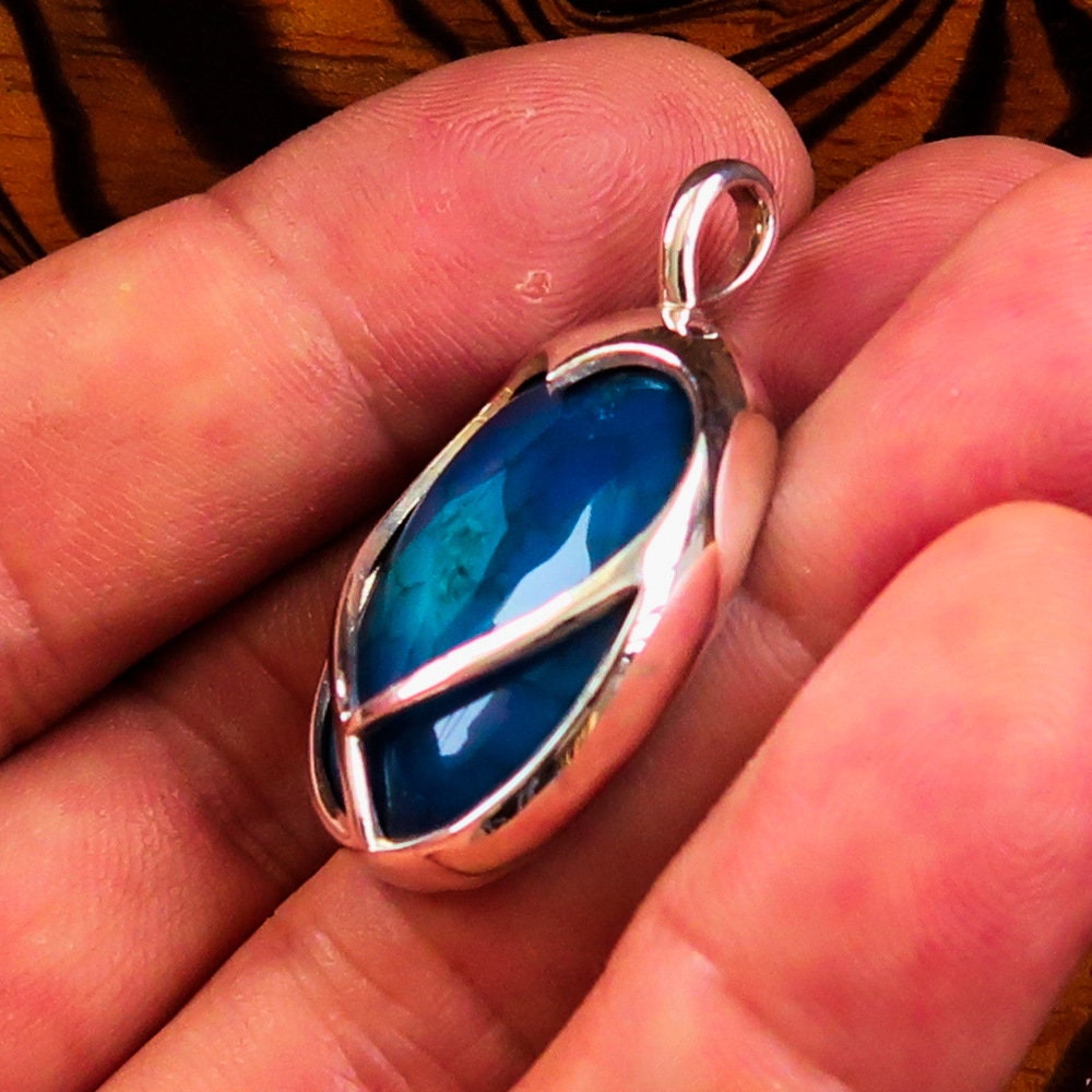 A beautiful heart-shaped sterling silver pendant featuring a blue agate cabochon, showcasing intricate craftsmanship and elegant design.