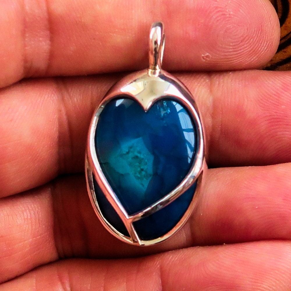 A beautiful heart-shaped sterling silver pendant featuring a blue agate cabochon, showcasing intricate craftsmanship and elegant design.