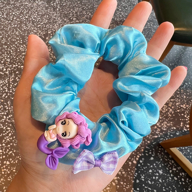 A vibrant Mermaid Blue Hair Tie featuring a woman holding blue hair ties with cute mermaid designs, perfect for whimsical hairstyles.