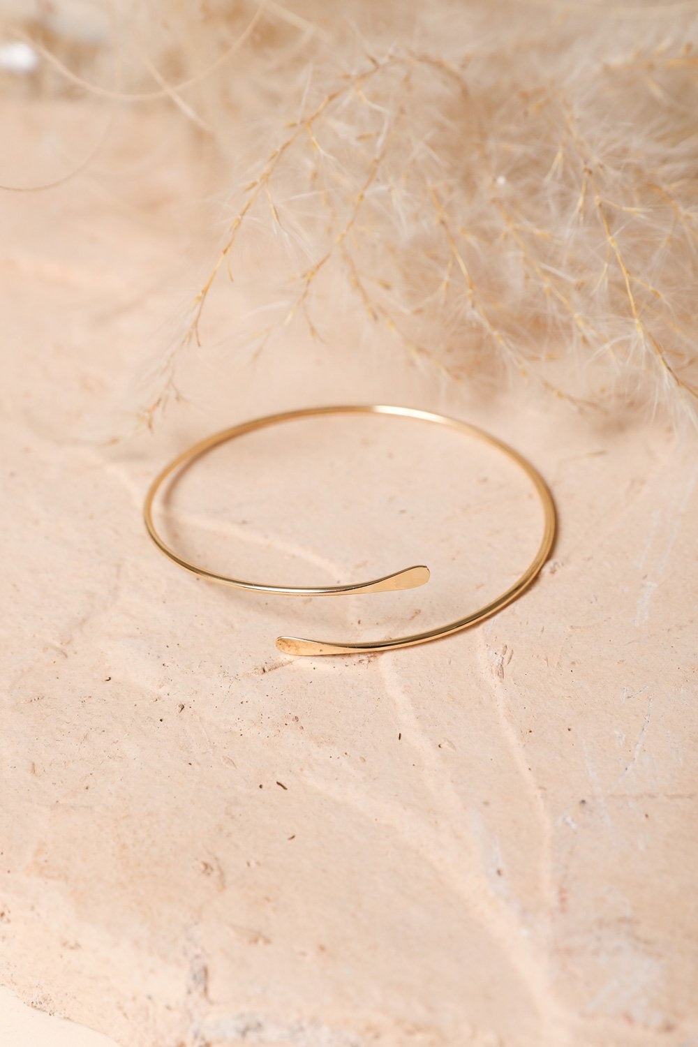 A chic Minimal Arm Cuff/Bangle in hammered gold design, elegantly hanging on a wrist, showcasing its minimalist style.