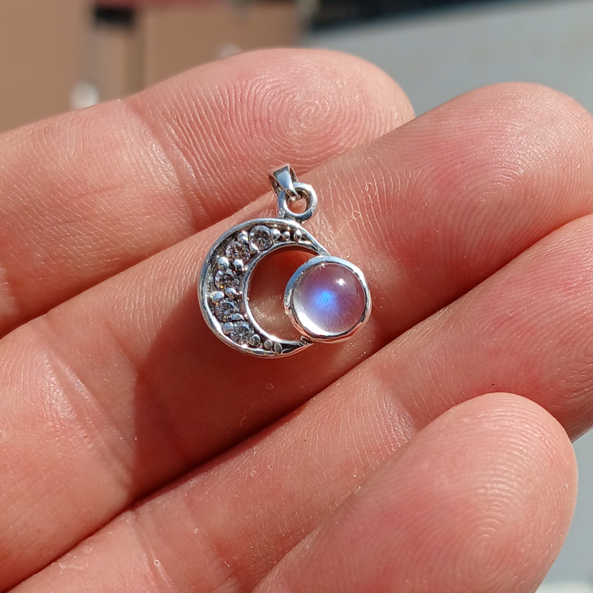 A beautiful crescent moon pendant made of sterling silver, featuring a central Ceylon moonstone and five sparkling cubic zirconias, showcasing elegance and charm.