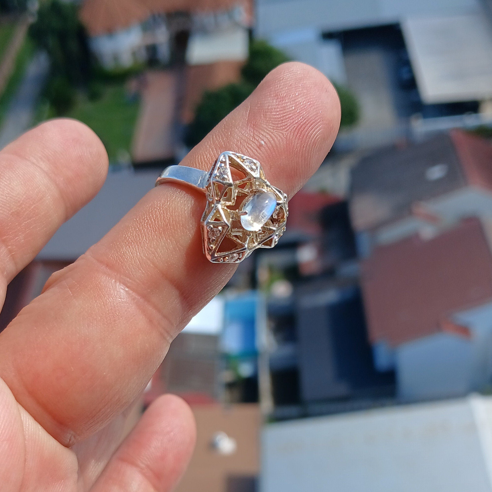A polished sterling silver ring featuring an oval moonstone, designed in a unique triangle shape, showcasing its elegant craftsmanship.