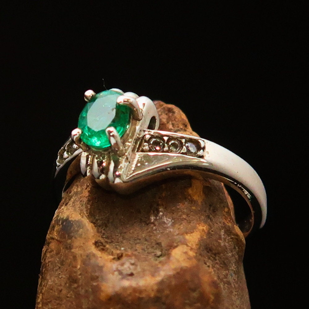 A stunning handmade sterling silver ring featuring a natural oval cut emerald gemstone surrounded by sparkling cubic zirconia stones.