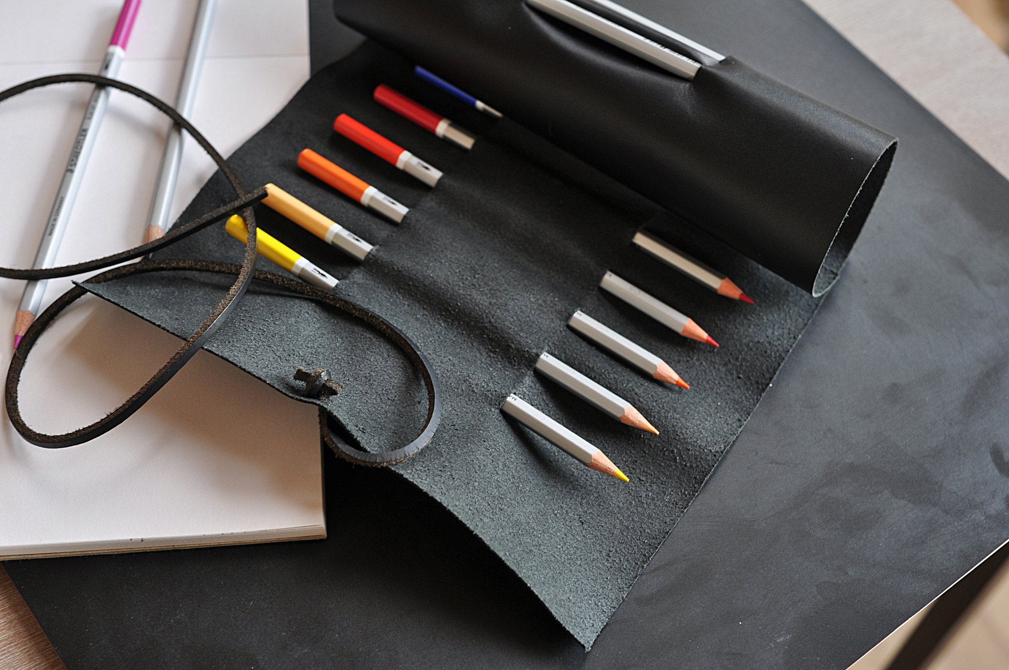 A stylish Pencil Wrap made from full grain cowhide leather, featuring 10 slots for pencils and pens, secured with a leather string closure.