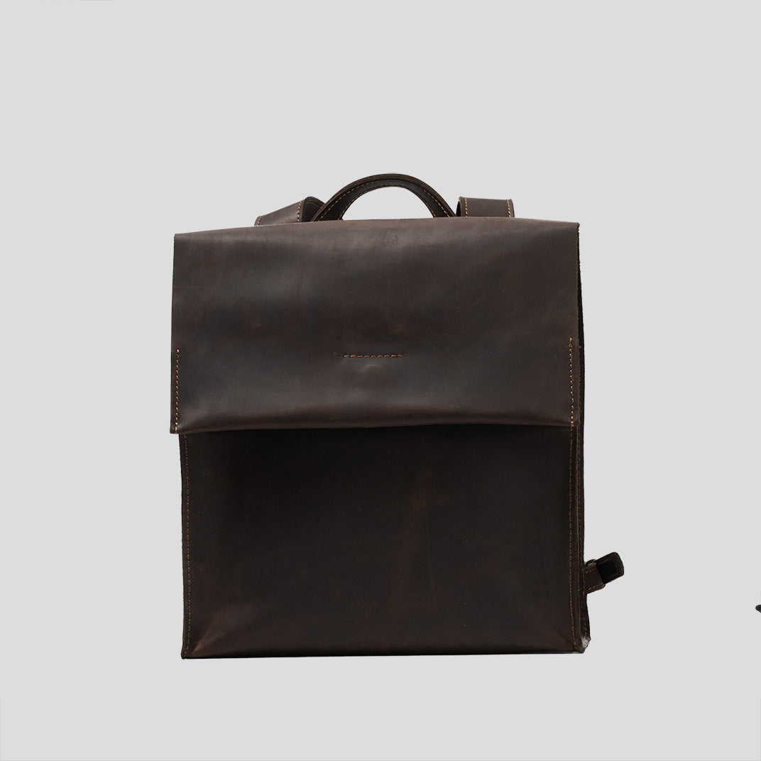 Dark brown leather backpack with minimal design, featuring adjustable straps and external zipper pocket.