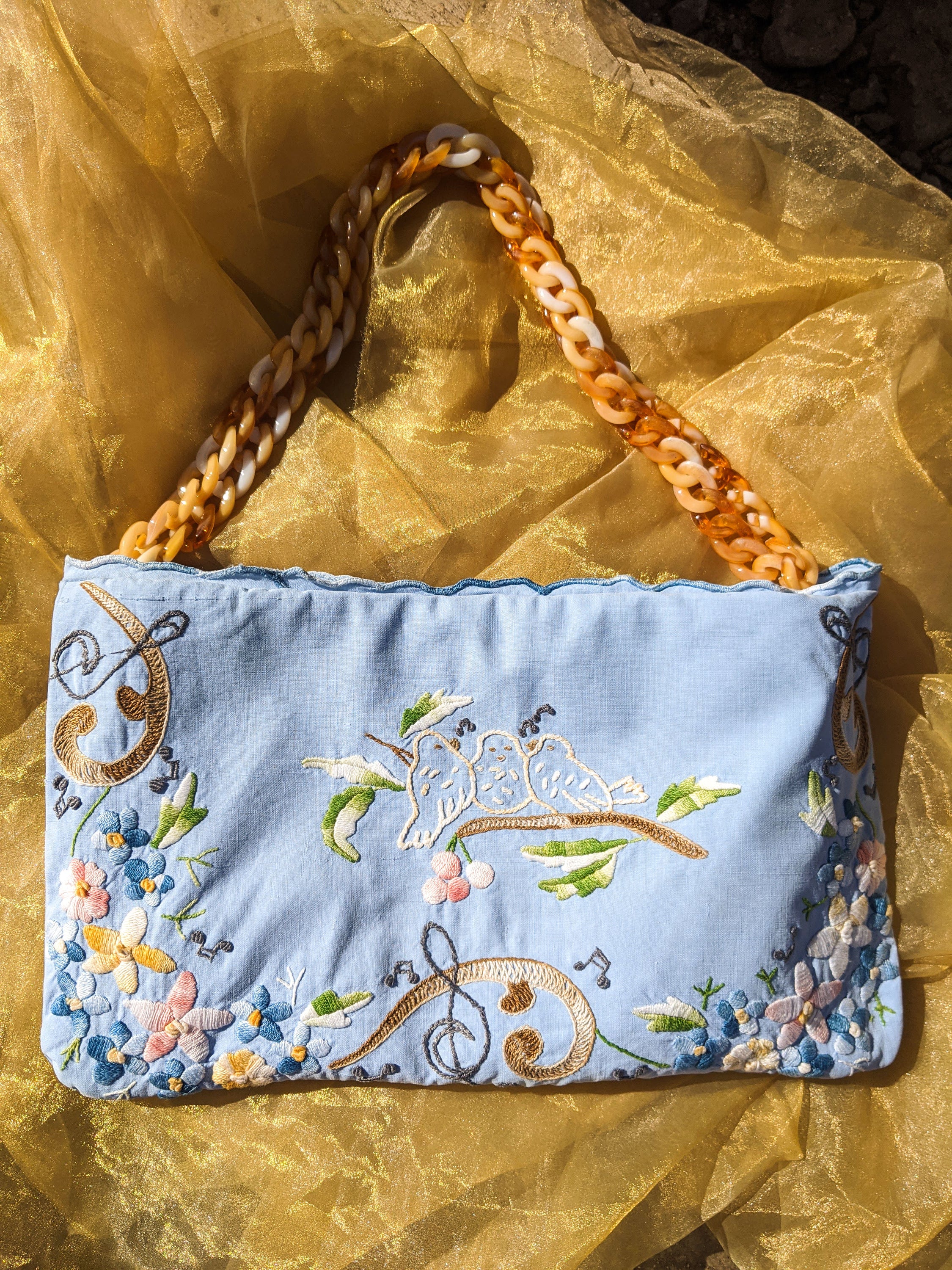 A blue antique garment cloth bag featuring intricate embroidered ornaments and a brown chain handle, showcasing its elegant design and zip closure.