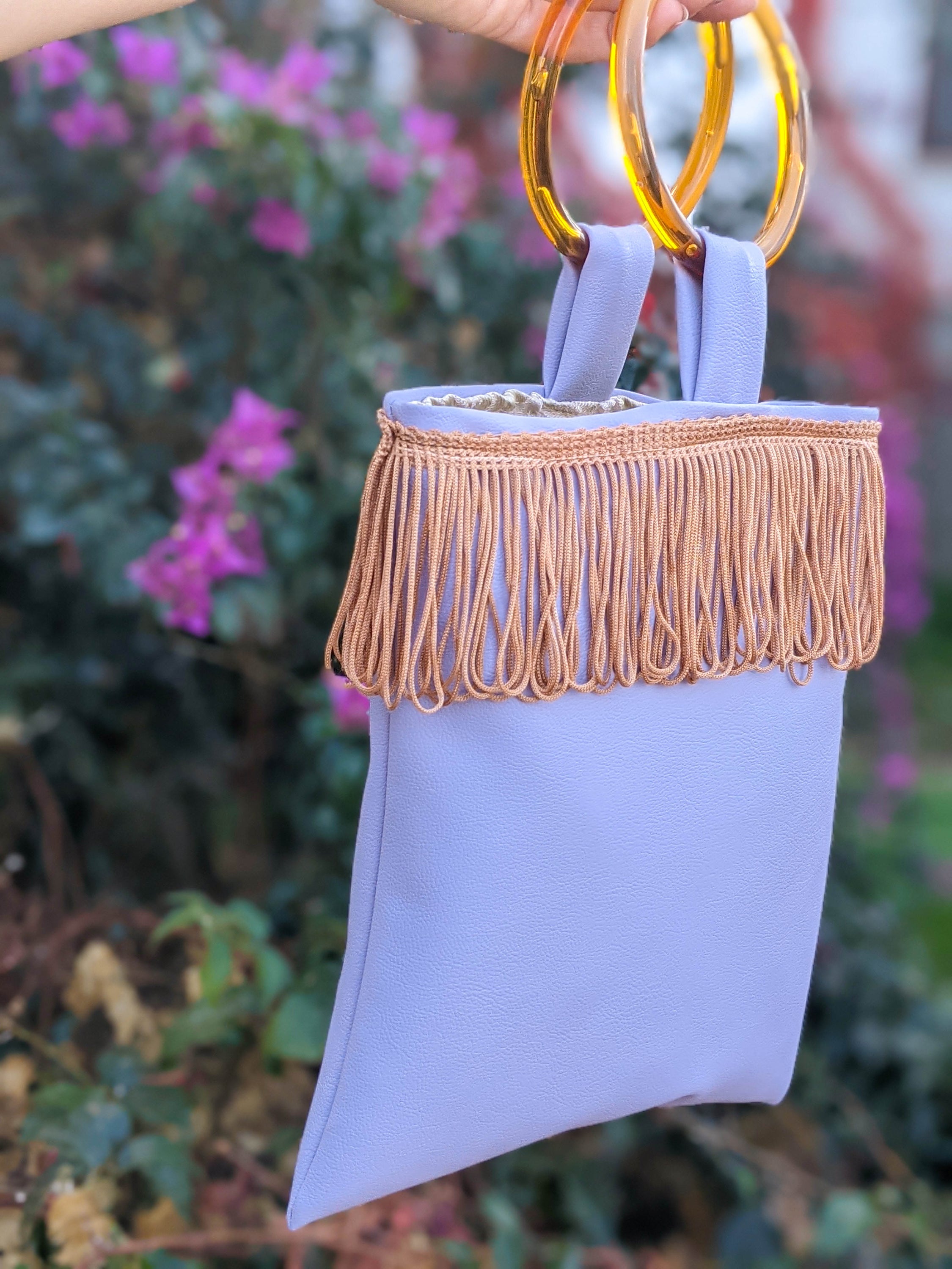Lilac mini faux leather bag with amber resin handles and brown fringes, showcasing a stylish and trendy design.