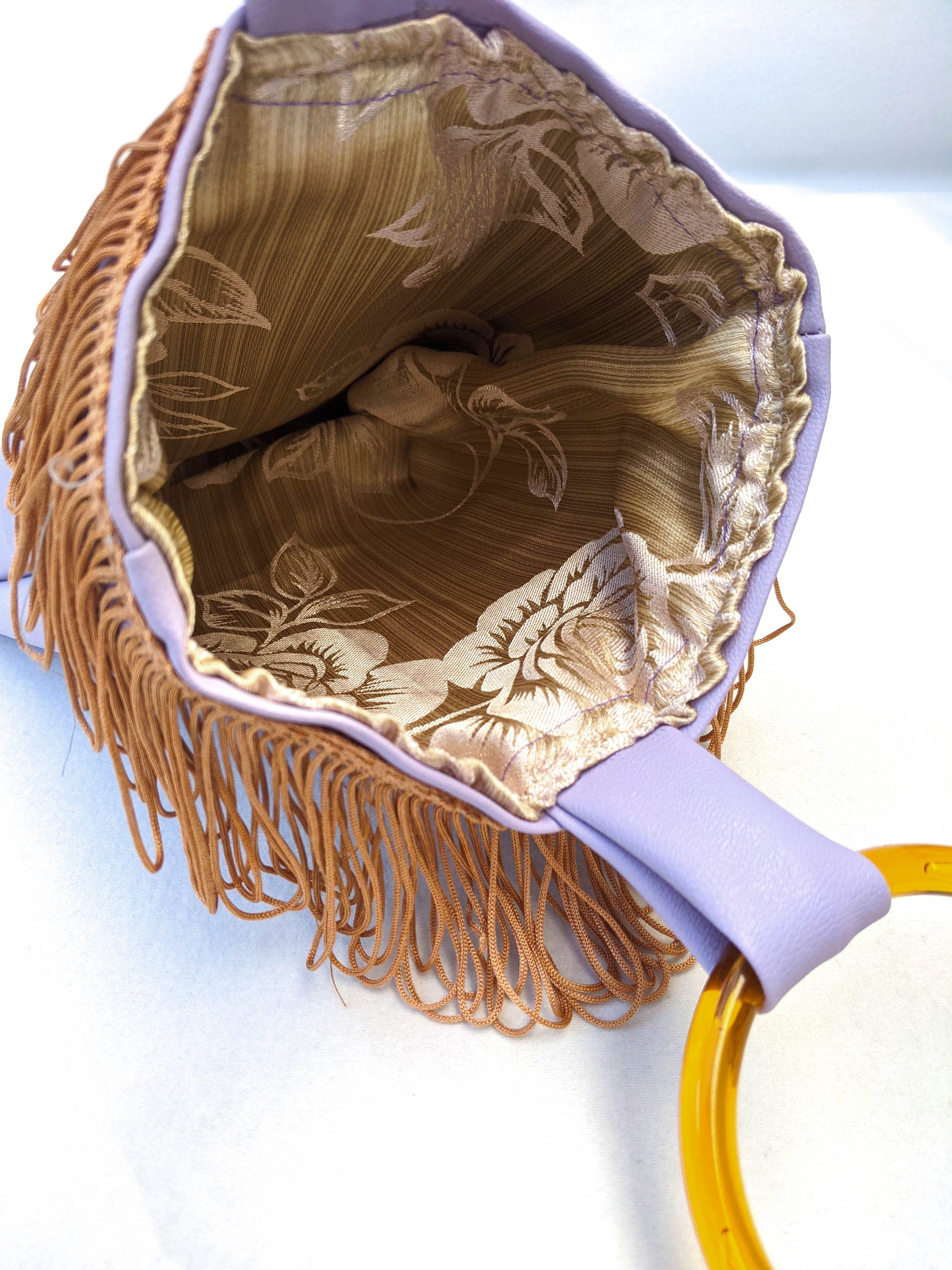 Lilac mini faux leather bag with amber resin handles and brown fringes, showcasing a stylish and trendy design.