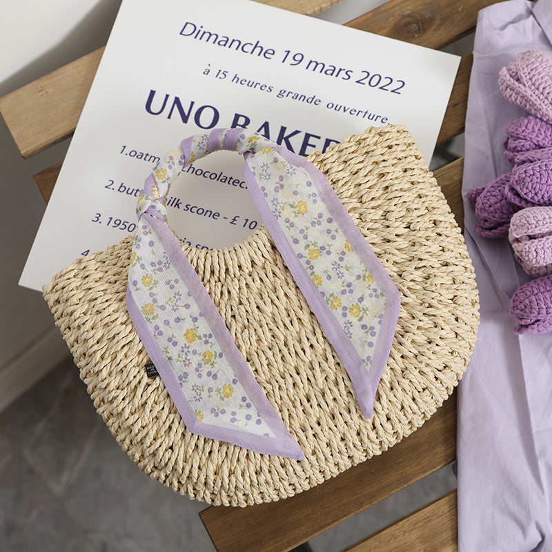 SolunaWeave™ Petite Bloom Bag featuring handwoven lavender and cream straw with a floral silk scarf, perfect for elegant outings.