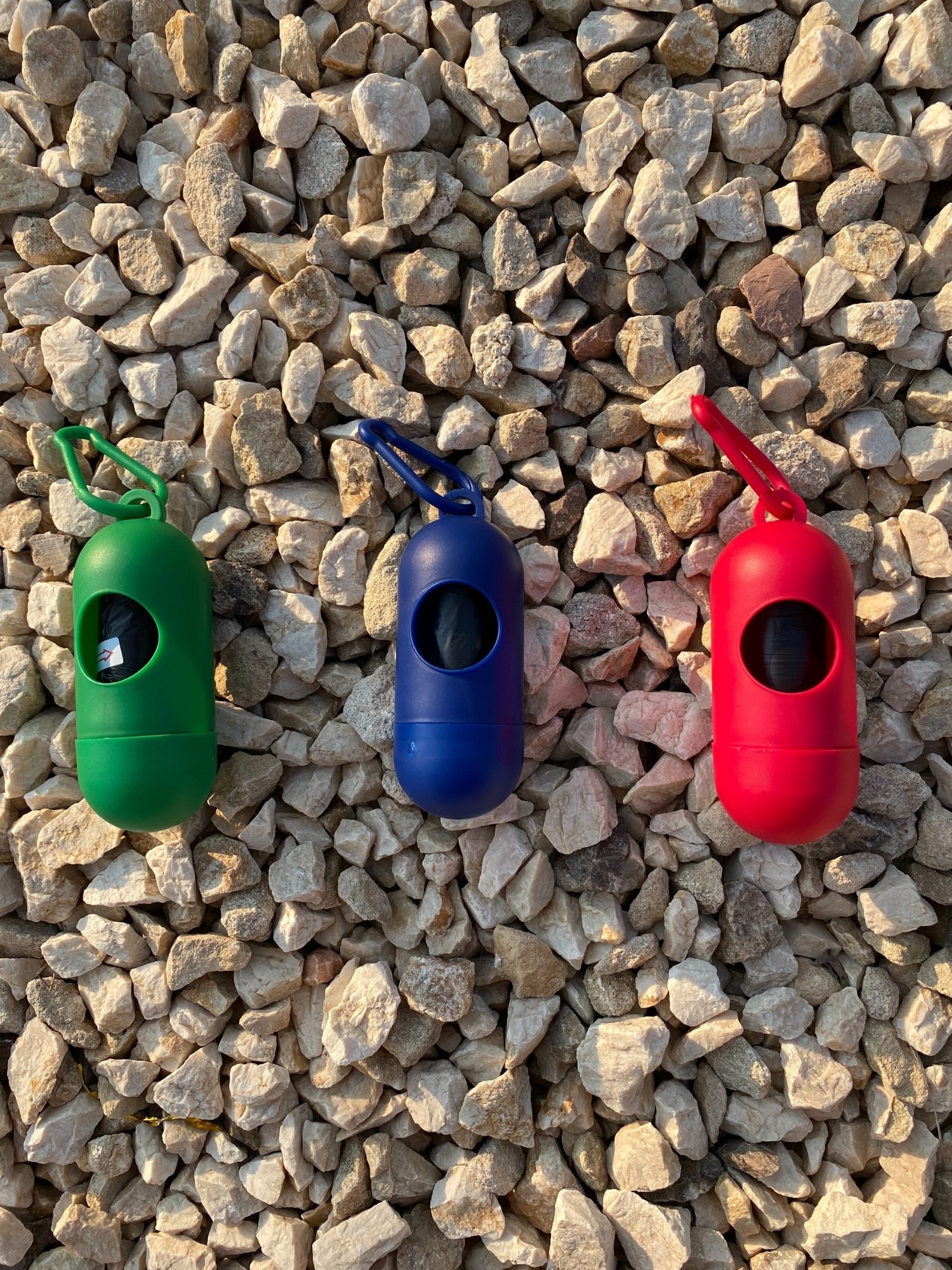 Dog Poop Bag Dispenser in vibrant colors with bags attached, showcasing its compact design and carabiner clip.