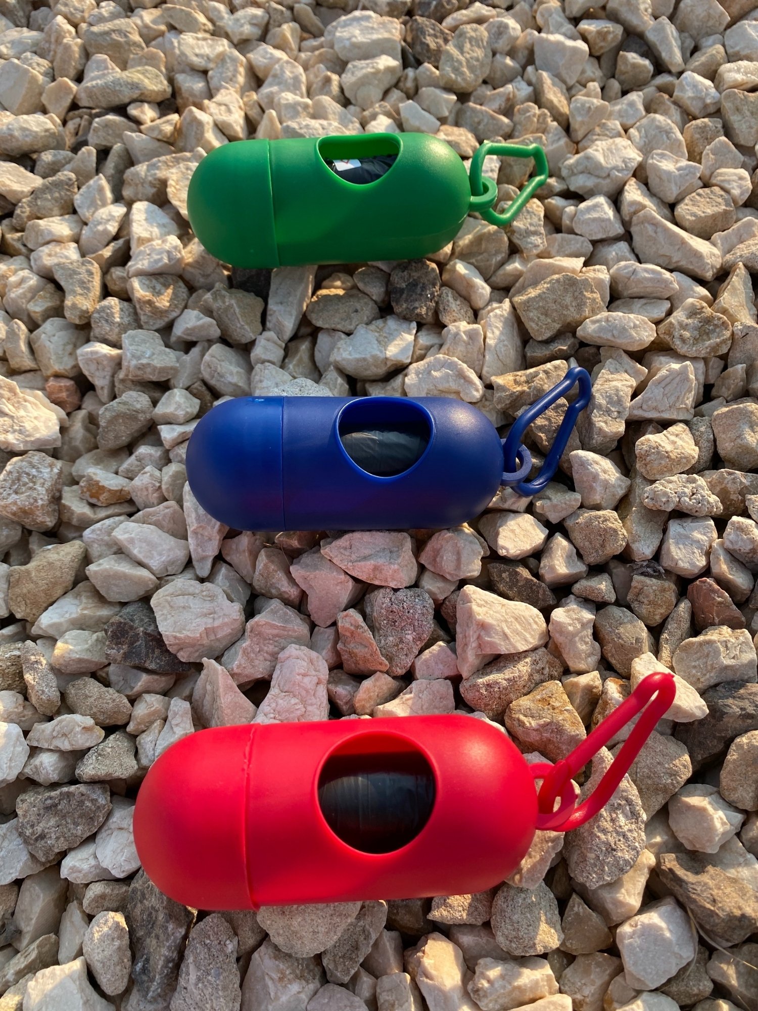 Dog Poop Bag Dispenser in vibrant colors with bags attached, showcasing its compact design and carabiner clip.