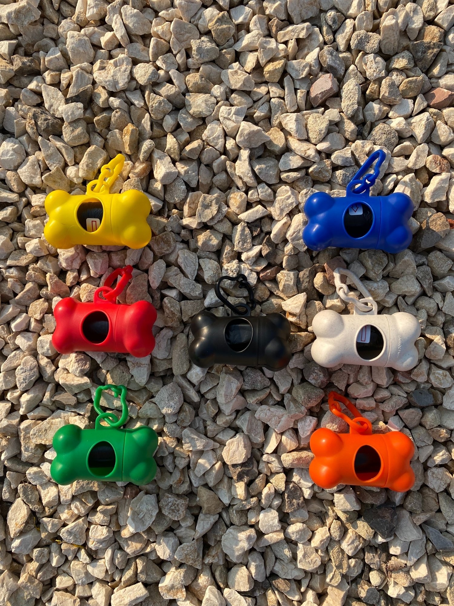 DogBone Poop Bag Dispenser in various colors with attached bags, featuring a plastic carabiner clip for leash attachment.