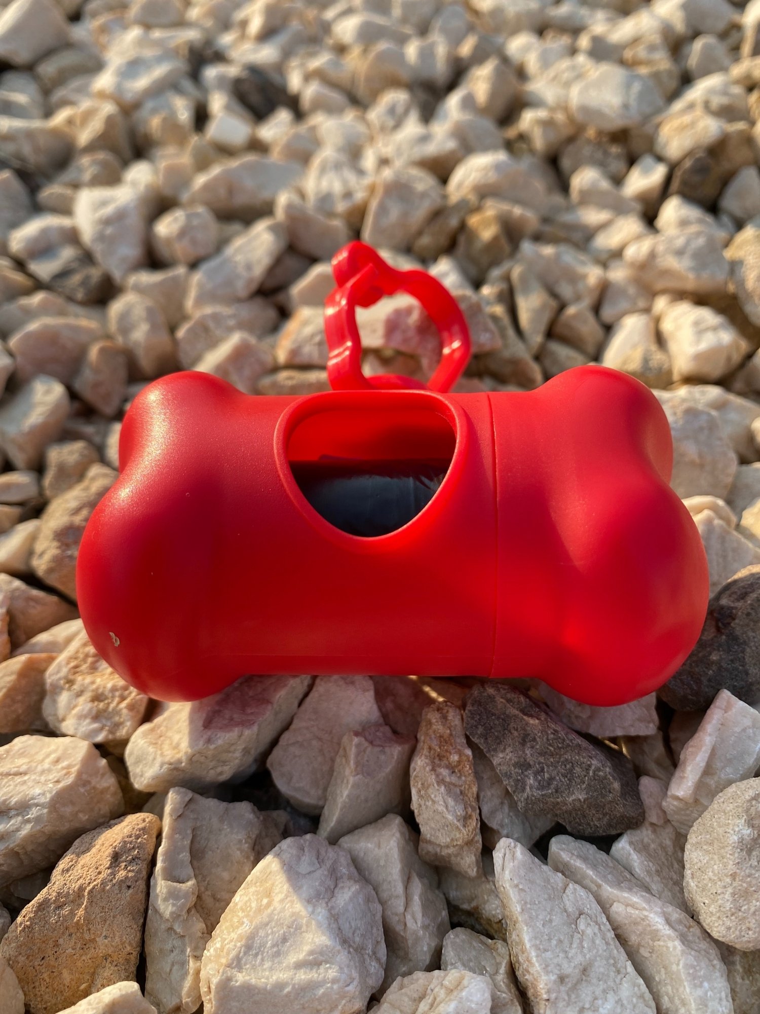 DogBone Poop Bag Dispenser in various colors with attached bags, featuring a plastic carabiner clip for leash attachment.