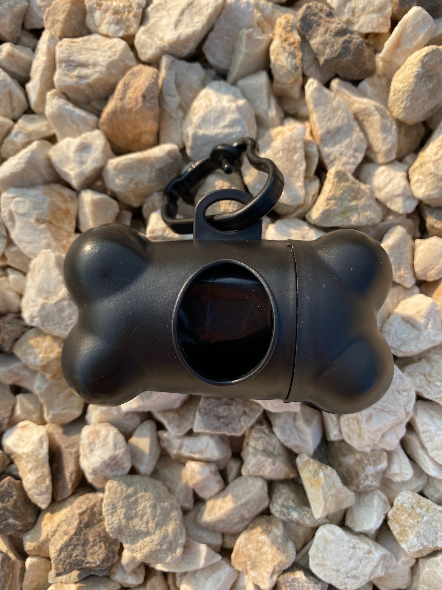 DogBone Poop Bag Dispenser in various colors with attached bags, featuring a plastic carabiner clip for leash attachment.