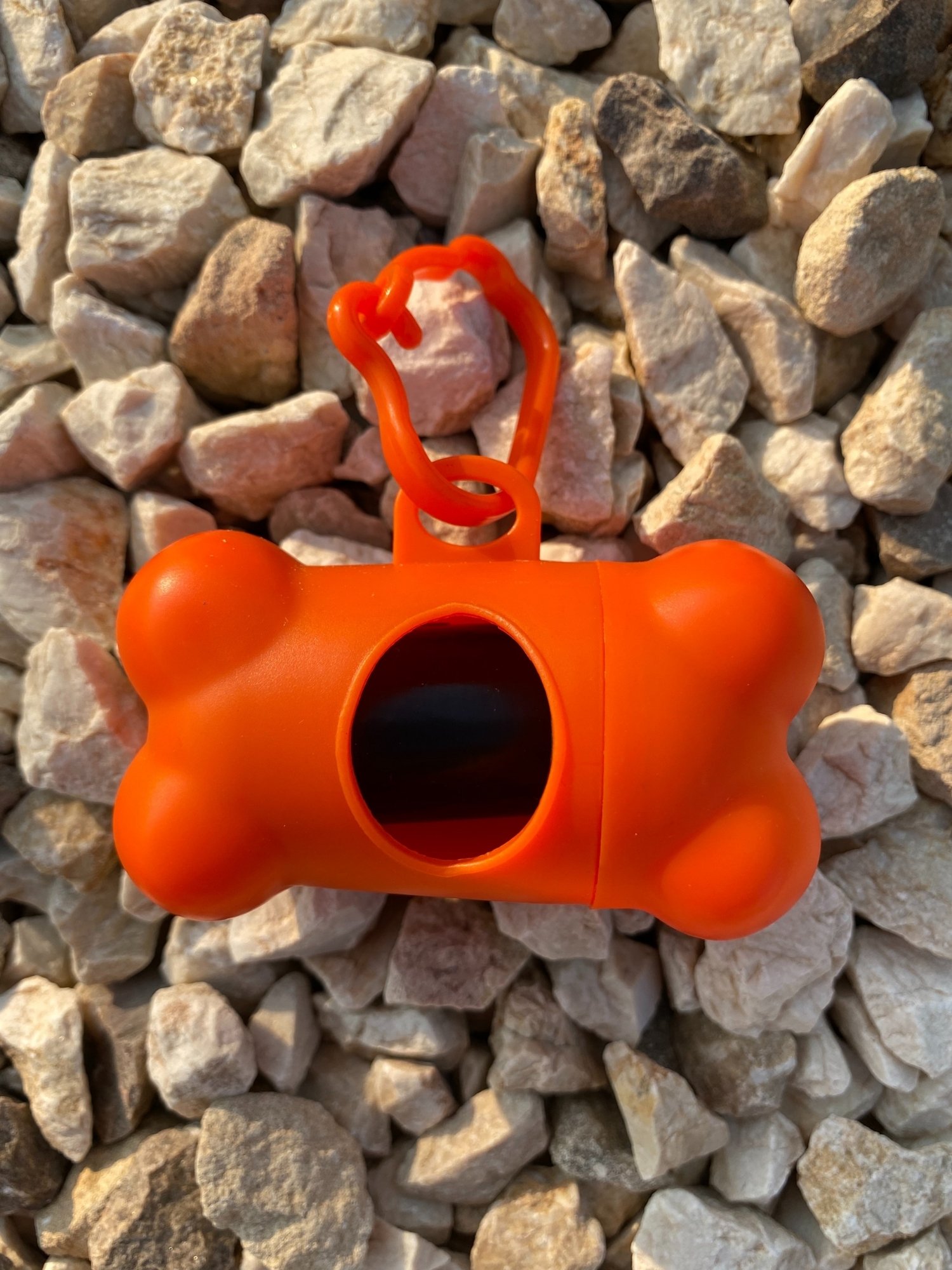 DogBone Poop Bag Dispenser in various colors with attached bags, featuring a plastic carabiner clip for leash attachment.