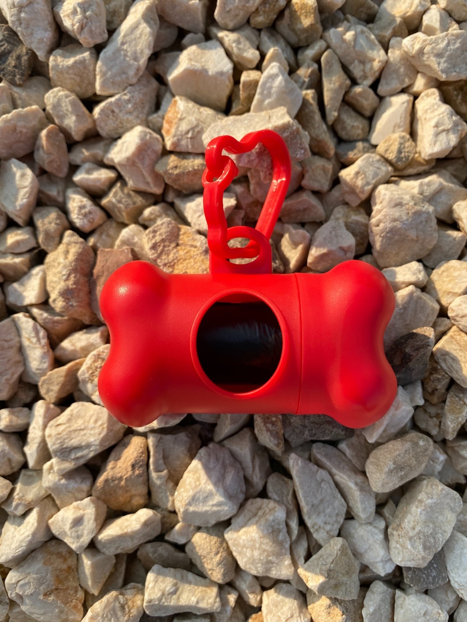 DogBone Poop Bag Dispenser in various colors with attached bags, featuring a plastic carabiner clip for leash attachment.