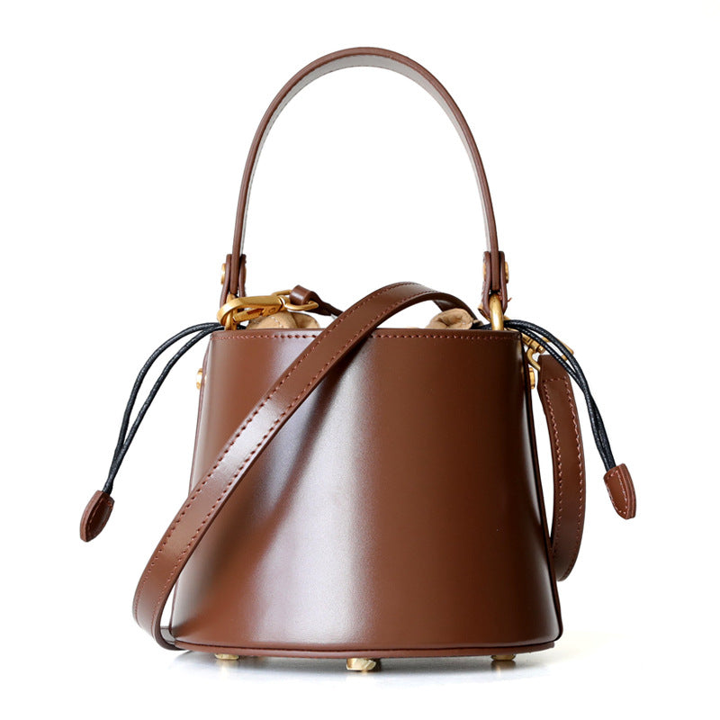A stylish leather mini bucket bag in apricot, caramel, and black colors, showcasing its elegant design and premium cowhide material.